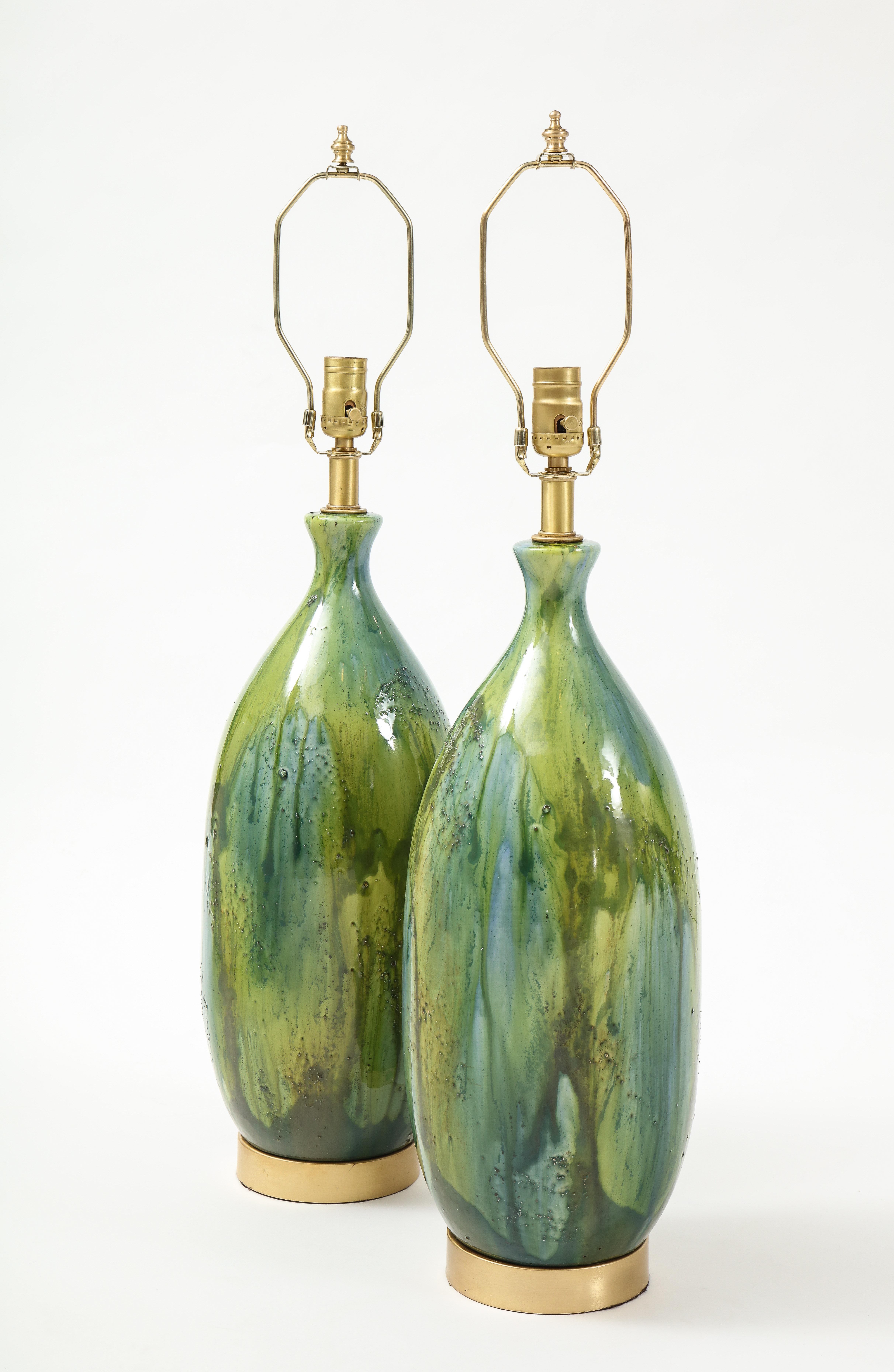 Pair of large scale bottle form ceramic lamps glazed in water and nature tones of blues and green sitting on satin brass disc bases. Rewired using clear cord, 100W max bulbs. Colors reminiscent of a Claude Monet painting.