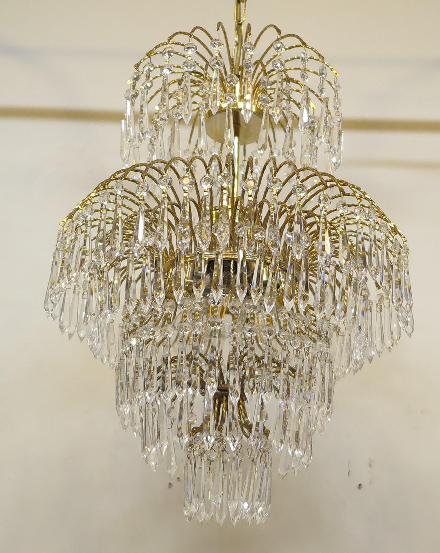 French Mid-Century Hollywood Regency waterfall chandelier with spectacular crystal prisms throughout. Features brass frame with steel gilded hangers with multiple cascading tiers floating drop cut crystals on brass fittings with crystal beads. The