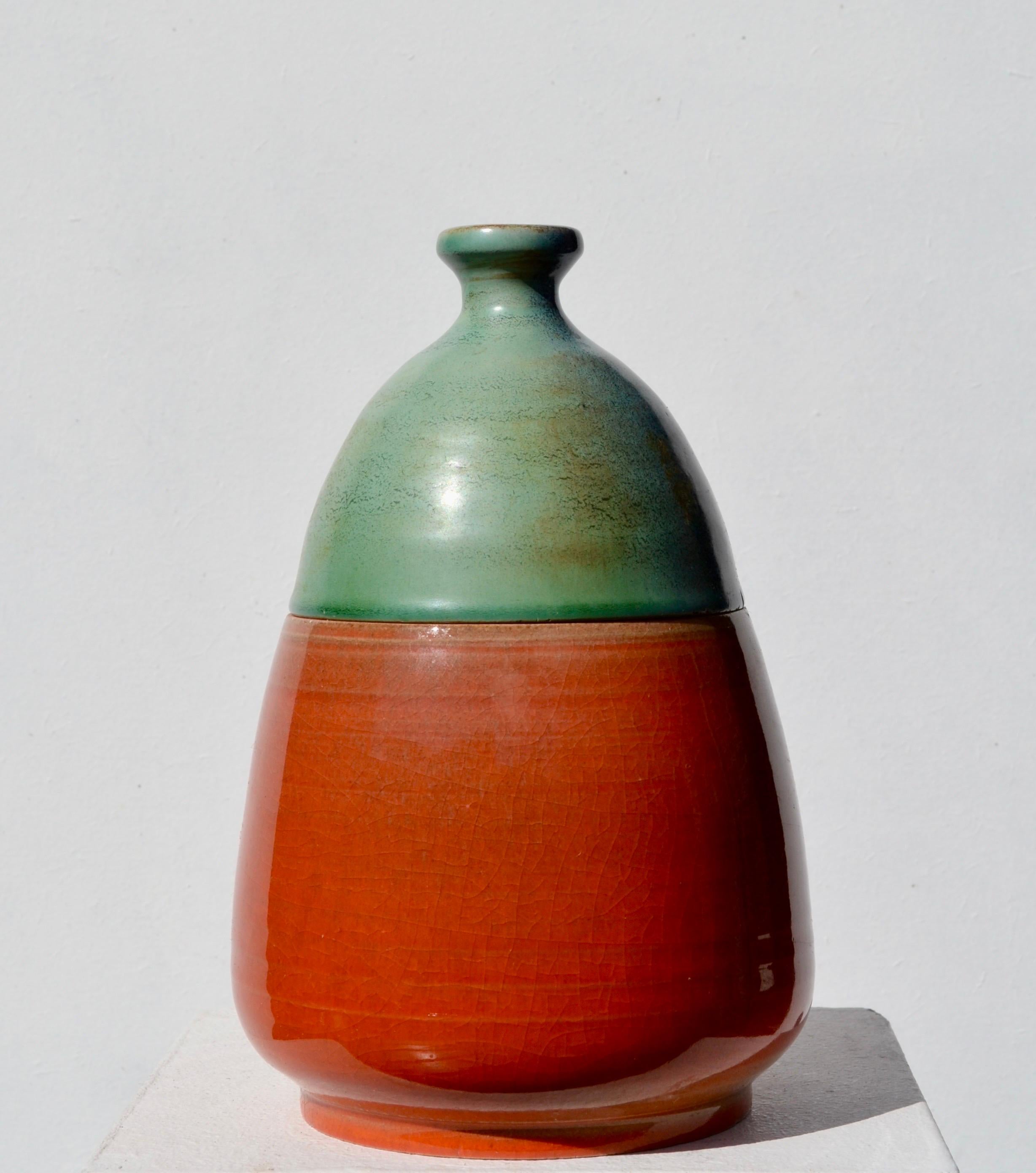Exemple frappant du design céramique français du milieu du siècle, ce pot à couvercle combine un corps rouge-orange audacieux avec un couvercle à l'émail vert doucement incurvé, réalisant un équilibre raffiné entre la forme et la couleur, typique
