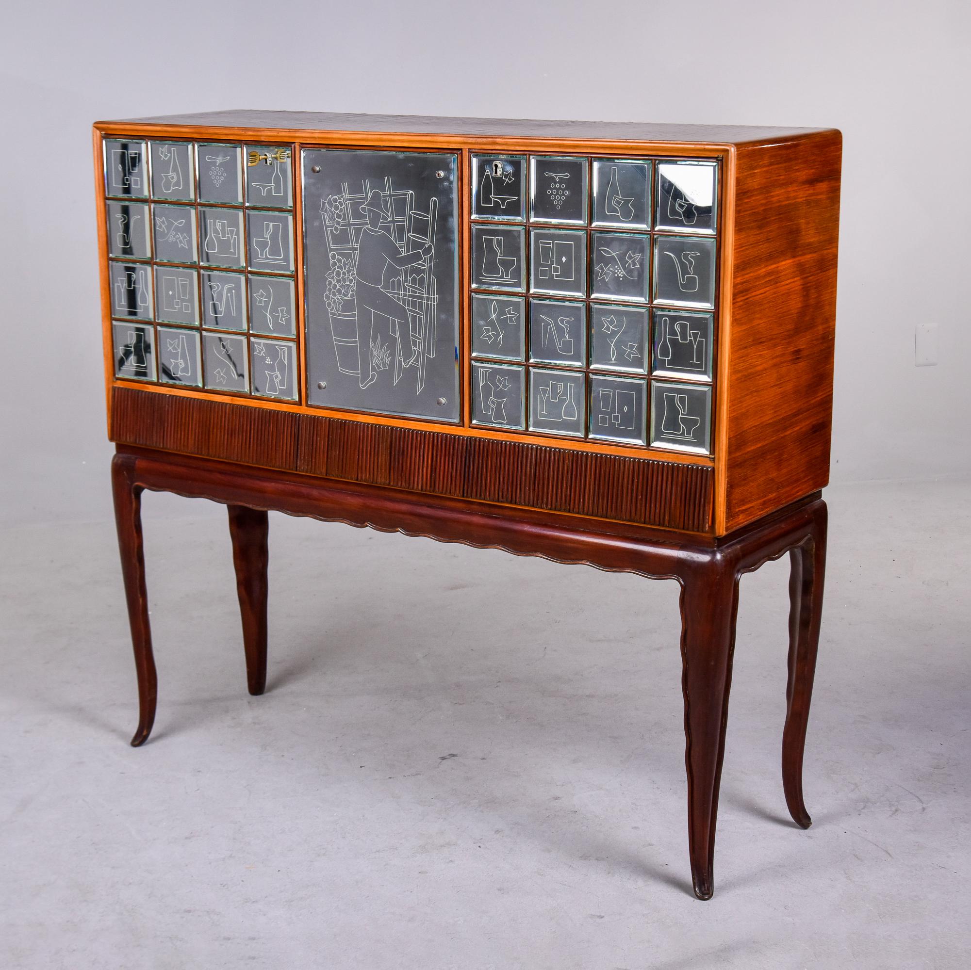 Found in France, this bar or liquor cabinet dates from the late 1940s / early 1950s. Made of mahogany with slender tapered legs, the cabinet has a subtle scalloped apron with reeded detail and three compartments covered in mirrored pieces etched