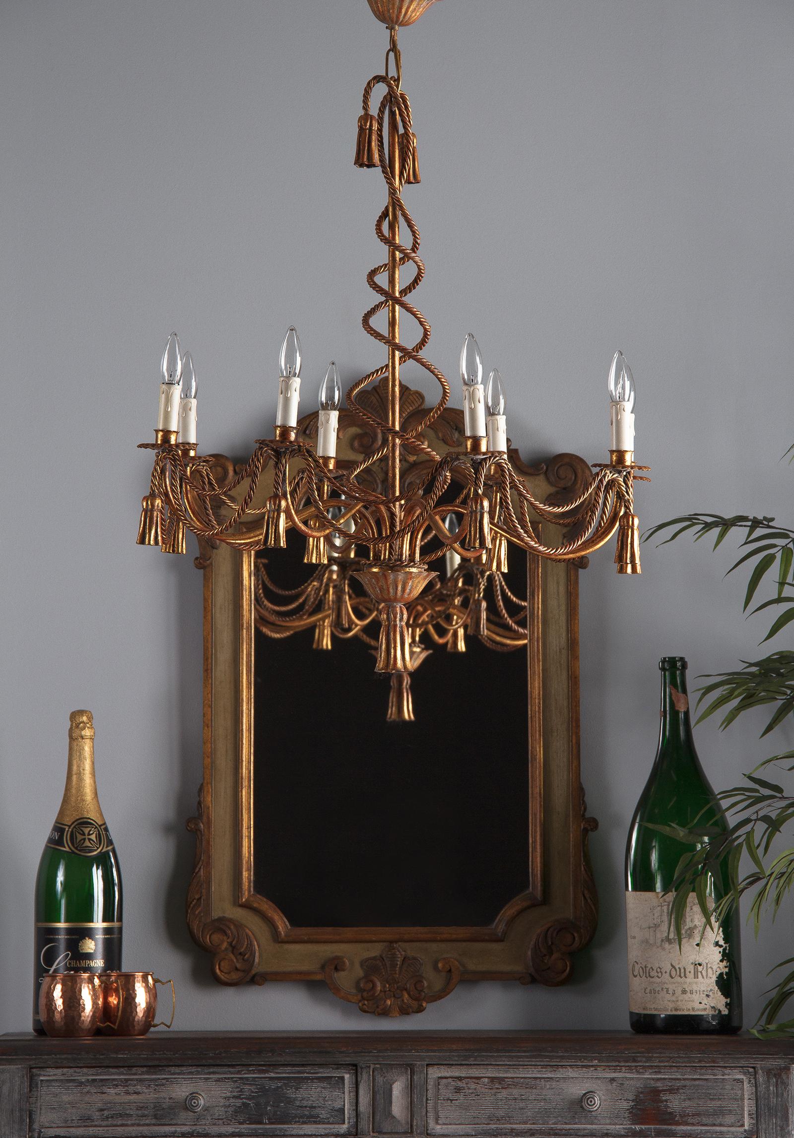 A gorgeous vintage gilt metal eight-light Louis XVI style chandelier, French midcentury. Eight undulating arms reach out from a centre post, each with a scalloped cup holding a faux candle light. Draping between each of the lights are two twisted