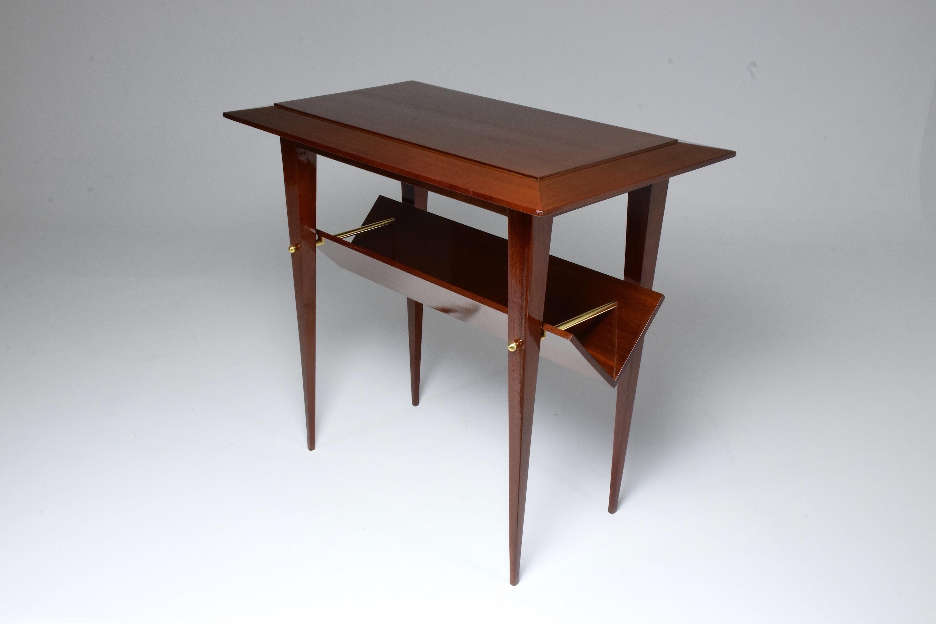 A timeless French 20th-century vintage high quality mahogany two-tier side or end table with tapered legs and brass details attributed to Raphael.
It is designed with an angular shaped shelf storage space dedicated to newspapers and magazines. An
