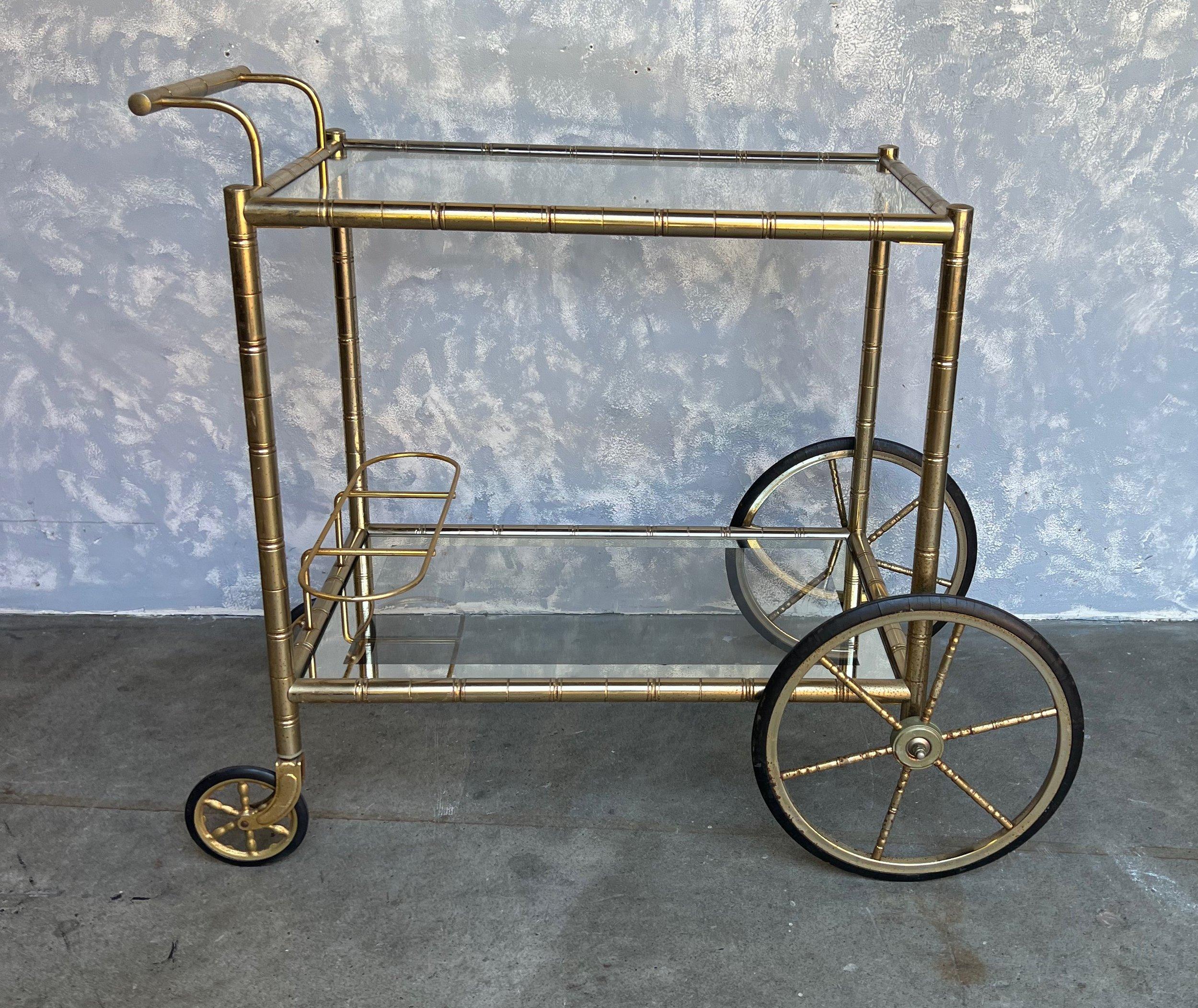 Cet élégant chariot de bar français en laiton et verre des années 1950 présente un cadre en laiton avec un motif de bambou stylisé. Il repose sur de grandes roues caoutchoutées à l'avant et de plus petites à l'arrière, avec une poignée permettant de