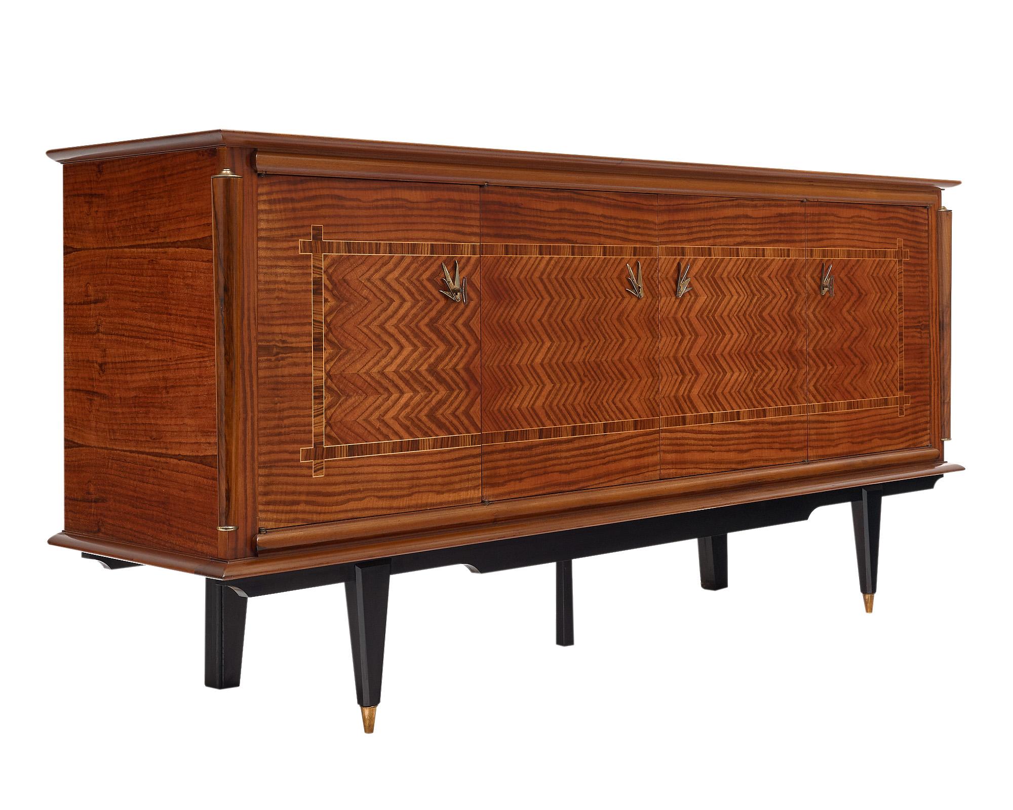 Credenza / Buffet from France. It is in the mid-century modern style with a striking chevron marquetry across the facade. The enfilade is supported by ebonized legs, the front two featuring brass feet. The four doors open up to interior shelving and