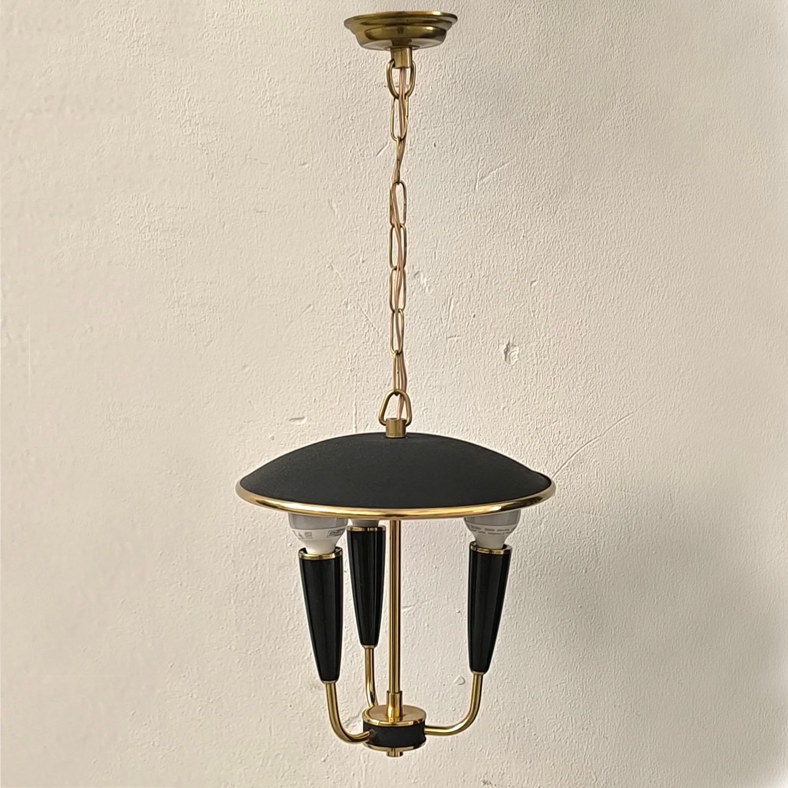 A Mid Century pendant lamp in a mixed textured surface.

The contrast of the gold brass and black is striking. The original colors are in good condition. Structural paint covers the top and bottom. Three radially arranged arms are below the
