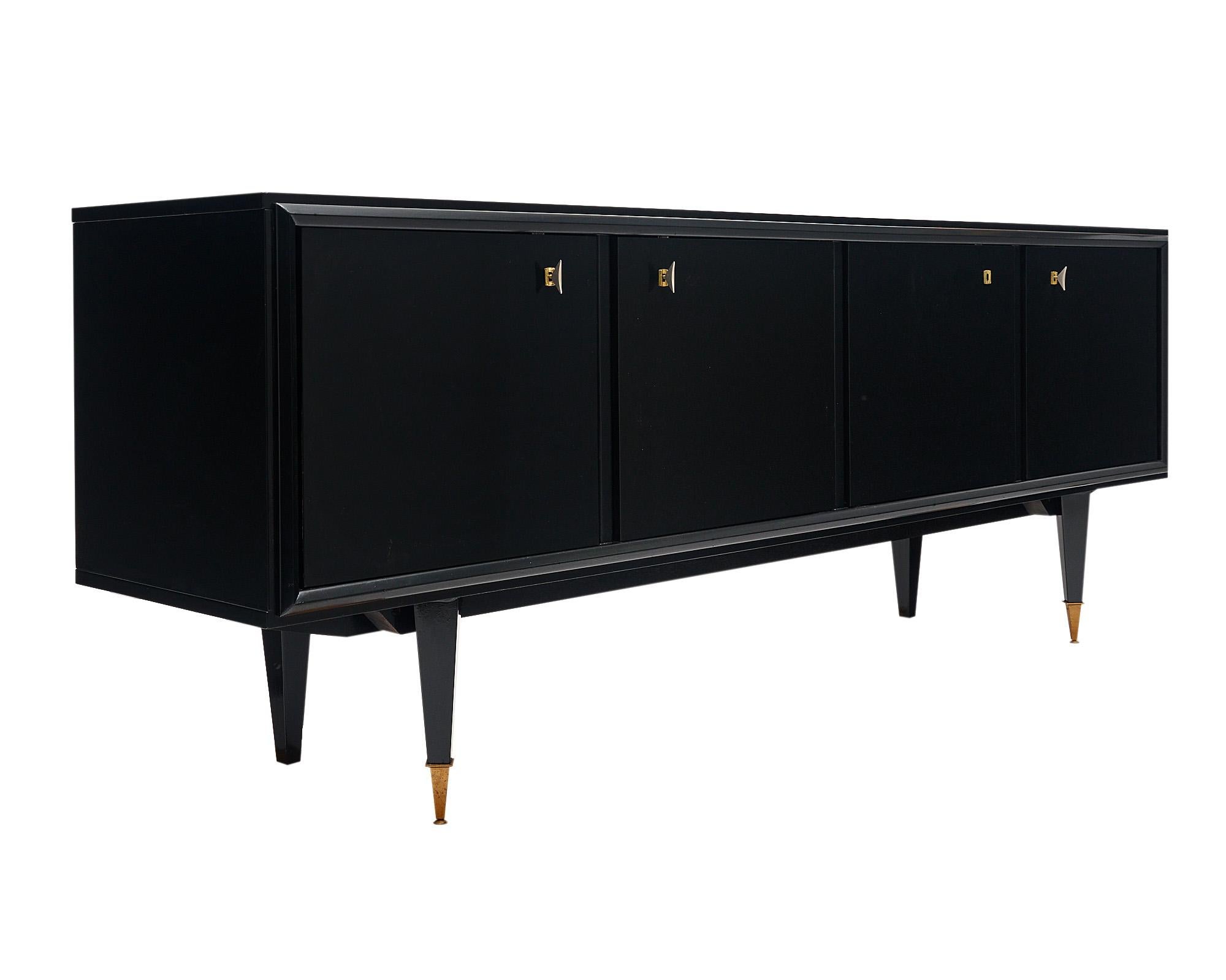 Buffet from the mid-century in France featuring tapered; geometric legs capped in brass and four doors with working keys and locks. The left most door opens to reveal a glass shelf and drawer; while the other doors reveal lemon wood interiors and
