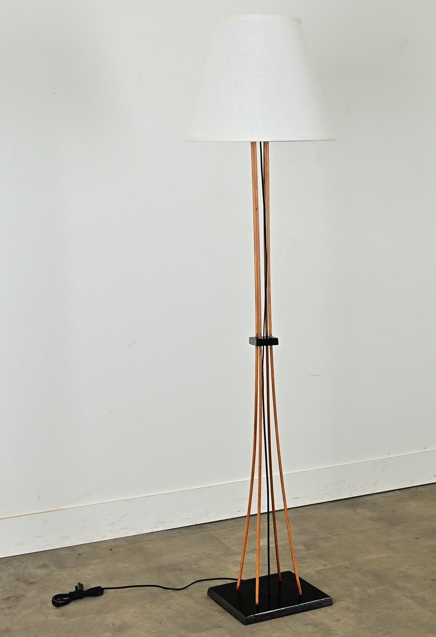 Una elegante lámpara de pie moderna de mediados de siglo con pantalla de lino blanco personalizada. Esta modesta luminaria tiene un diseño minimalista que incorpora cuatro esbeltos montantes de madera, arriostrados en el punto medio y en la parte