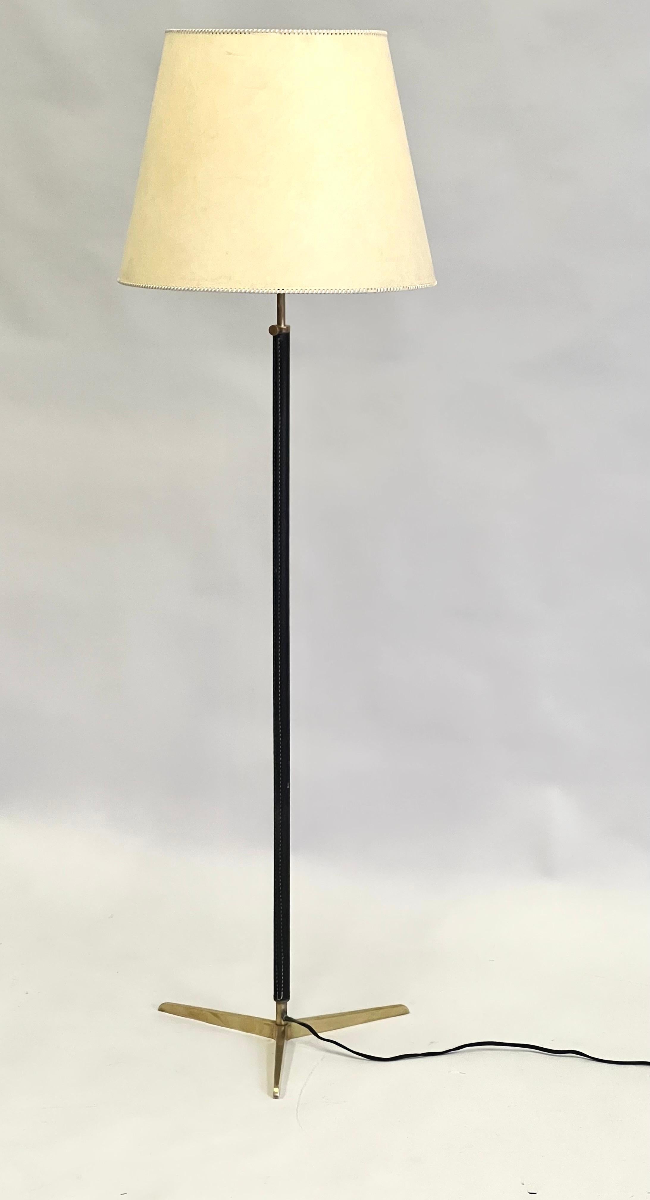 Elegant, modern and timeless french Mid-Century Modern hand-stitched leather and brass floor lamp attributed to Jacques Adnet. The lamp has a exquisite, pure form with its solid brass tripod base that is delicately tapered. The hand stitched black