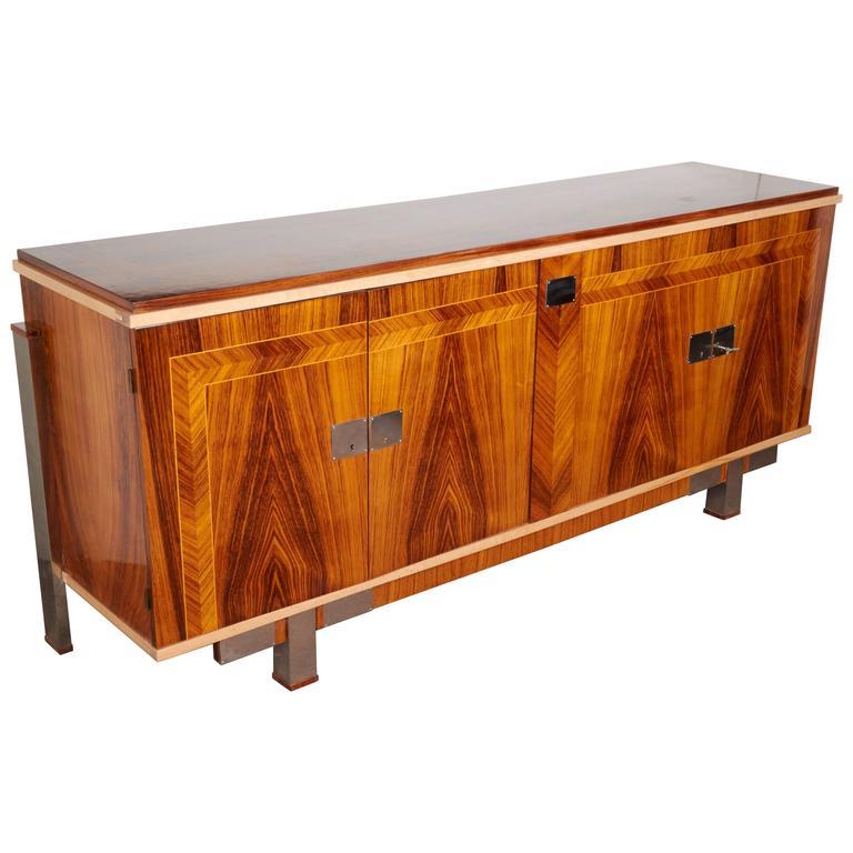 A gorgeous French Art Deco four-door sideboard featuring beautifully grained and bookmatched exotic palisander with blonde trim and parquetry detail, along with sleek nickeled bronze hardware. The cabinet is supported on a tall back tubular leg with