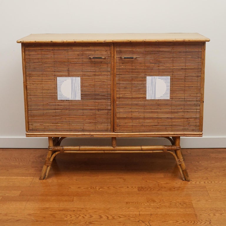 The French Mid-Century Modern rattan two-door server, shown here, is from the 1960s. It has been gently restored both inside and out and updated with modern tile insets. The brass handles are original to the piece. Great scale with ample storage.
