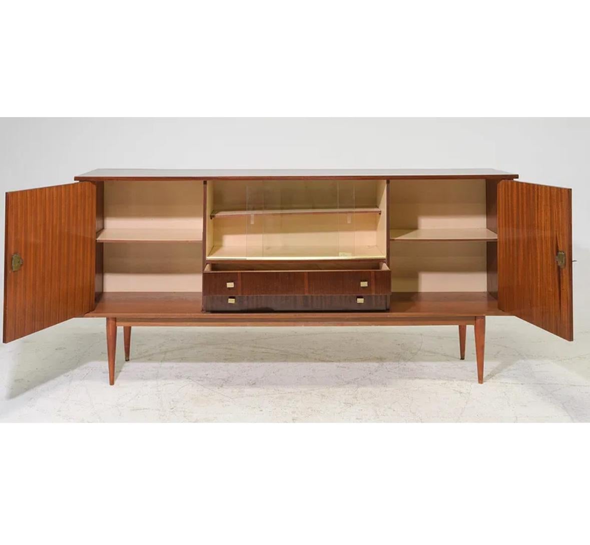 Also known as a credenza, this elegant sideboard features a sleek built-in bar cabinet that captures the spirit of the era. Designed with two doors revealing ample storage and two drawers for added functionality, it blends timeless style with