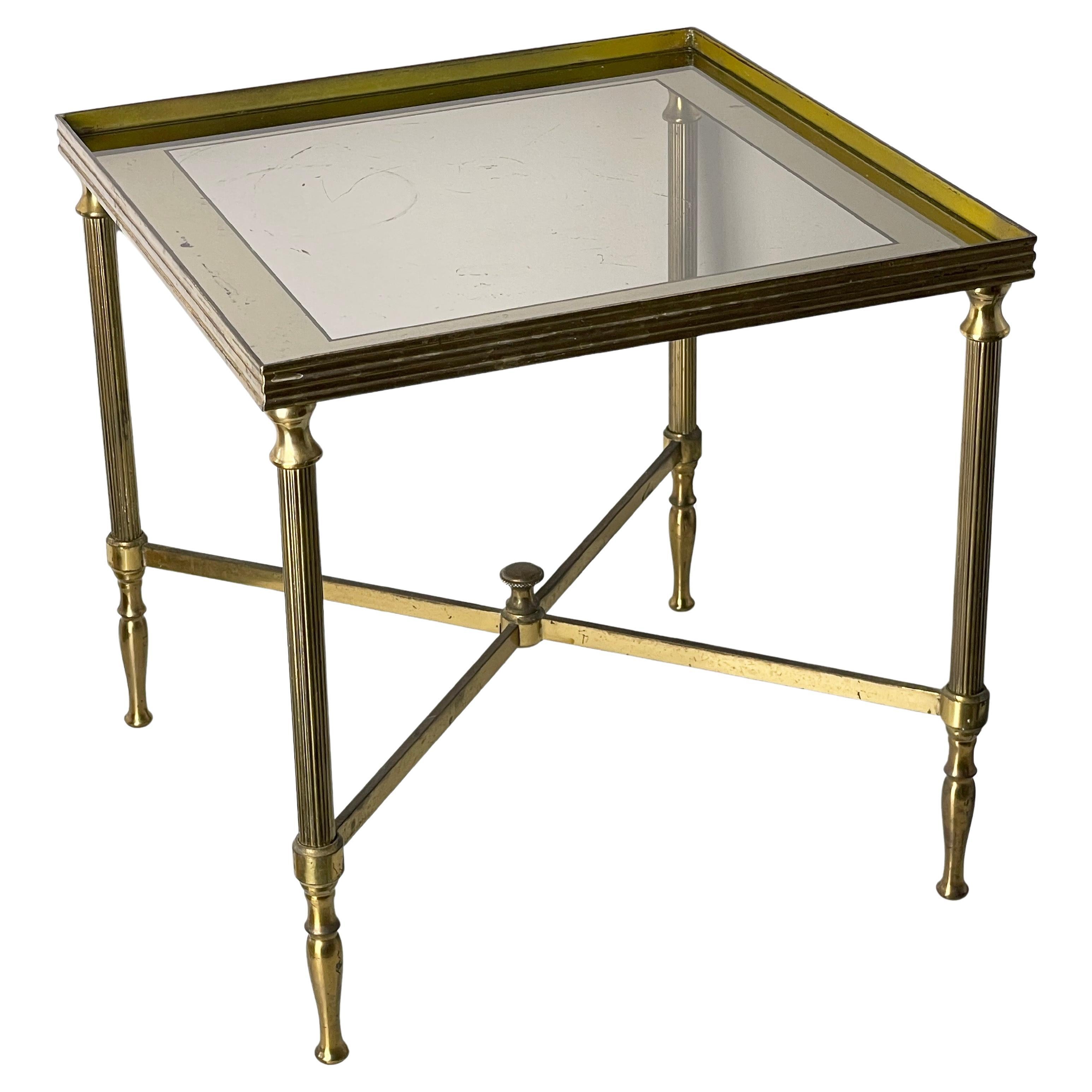 Table d'appoint en laiton de style néoclassique / Hollywood Regency du milieu du siècle, avec plateau en verre et bordures en miroir. La base est bien détaillée. Avec un niveau de patine et des signes d'utilisation correspondant à l'âge. 
Design/One