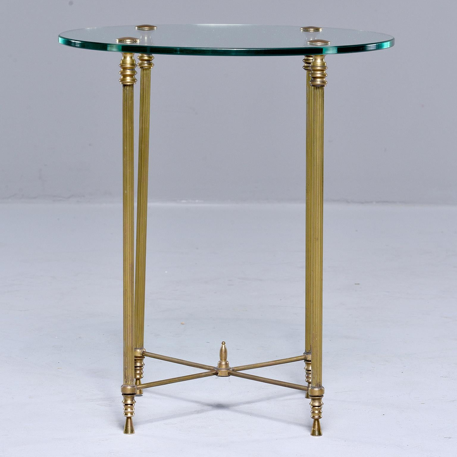 Small round side table found in France, circa 1960s. Round glass tabletop, x-form brass stretchers with a center finial and reeded brass legs. Unknown maker.
