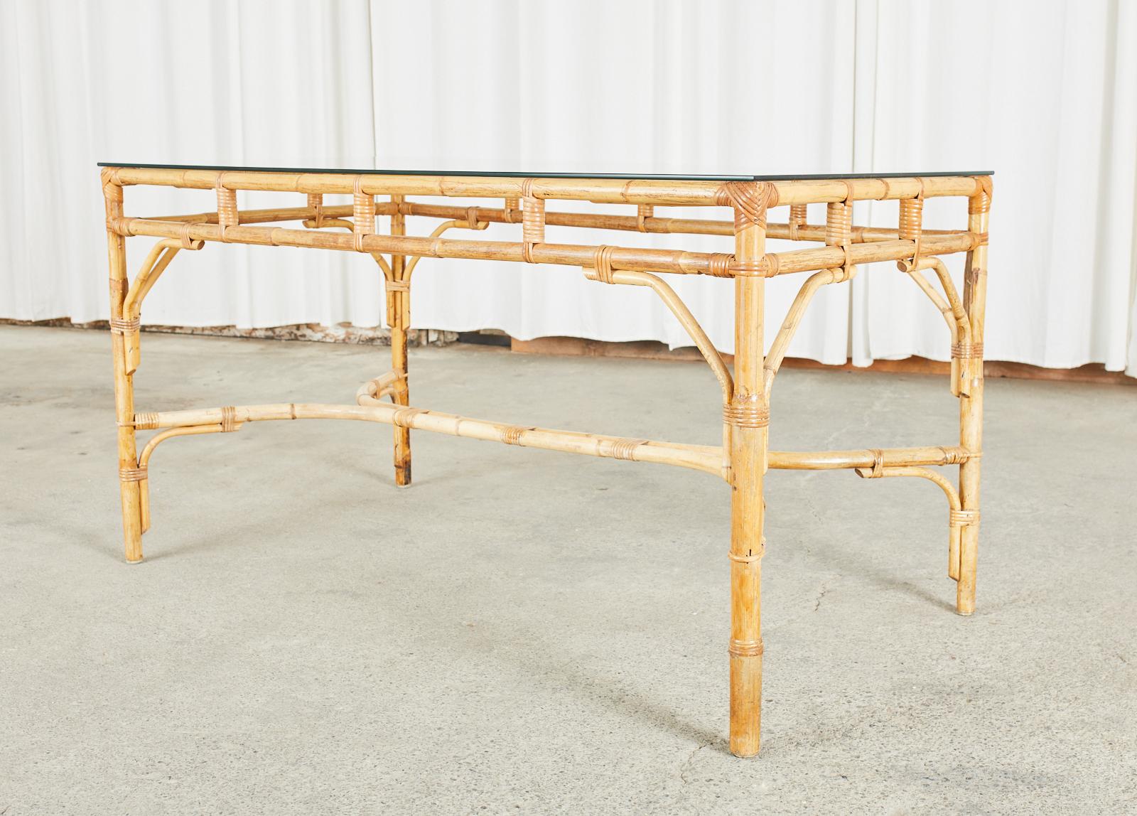 Stylish French Mid-Century Modern dining table crafted from bamboo in the organic modern style. The table features a rectangular bamboo pole frame lashed together with rattan wicker laces. The sides of the table have a decorative open fretwork apron