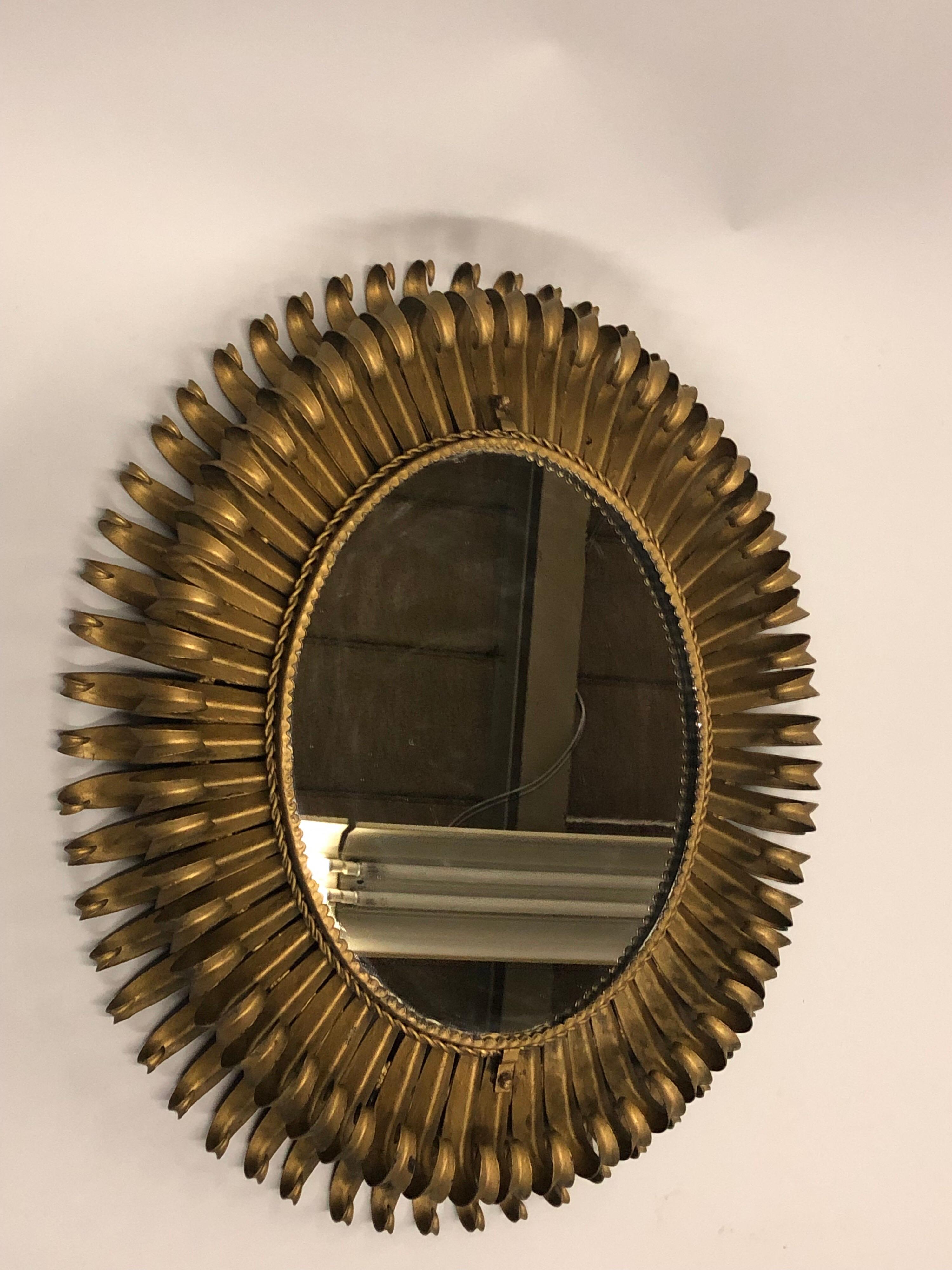 A Unique French Mid-Century Modern Neoclassical oval form wall / sunburst mirror with double level projections in the style of the French legendary ironworker of the 1940's: Gilbert Poillerat. The piece is dramatic and iconic with its double level