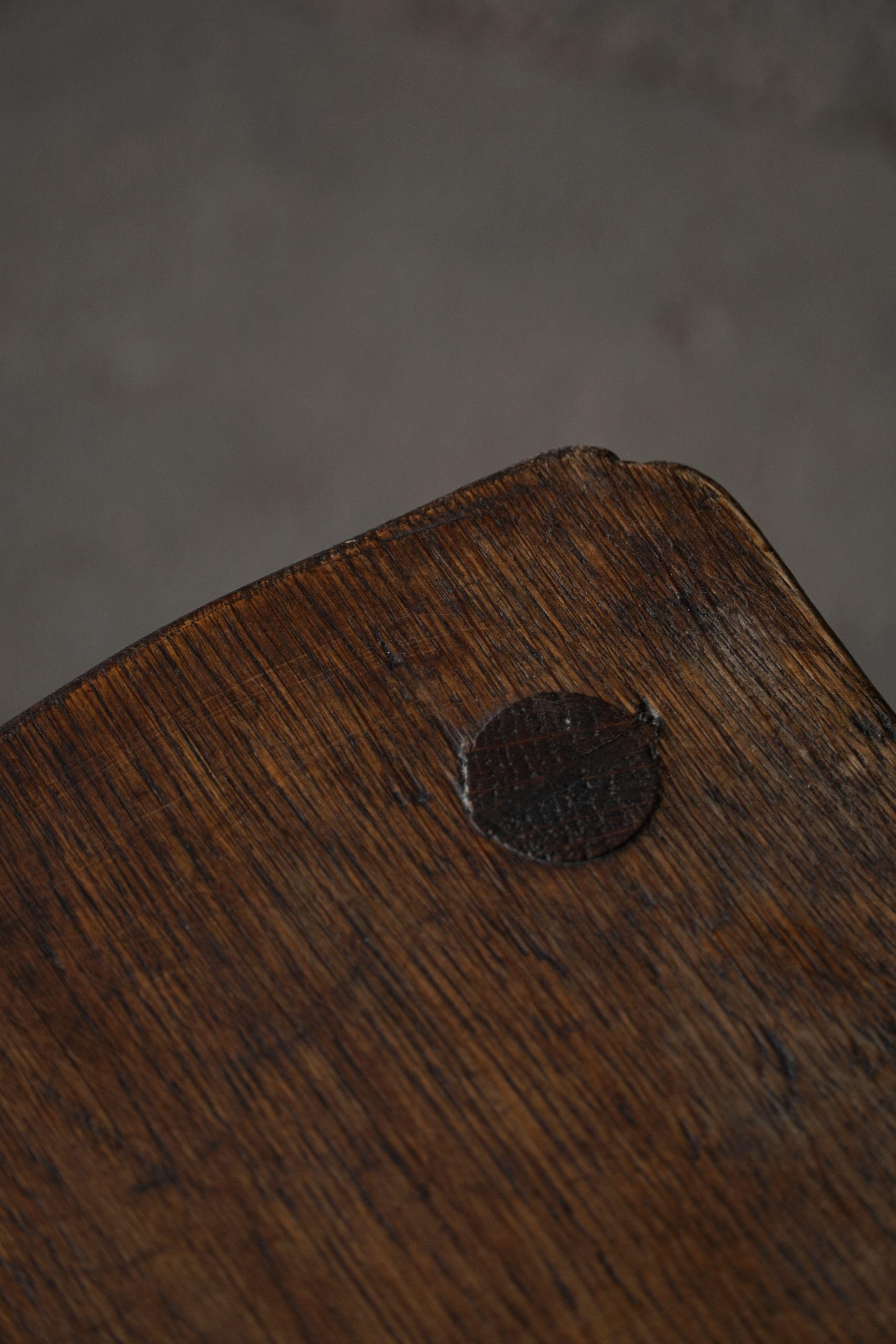 Ein wunderschön gearbeiteter französischer Hocker aus der Mitte des Jahrhunderts aus stark nachgedunkeltem Eichenholz, der sowohl elegantes Design als auch feine Handwerkskunst zeigt. Der Sitz aus massivem Eichenholz weist subtile, organische Kurven