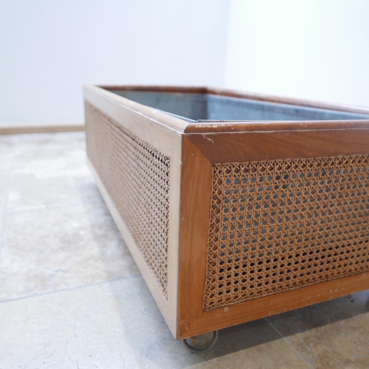 French, midcentury rattan planter. 

Ideal for home or office environment. 

Rattan side, wooden carcass, raised on metal wheels. 

Condition is generally good but there are scuffs to the wood. The internal metal soil container is solid and