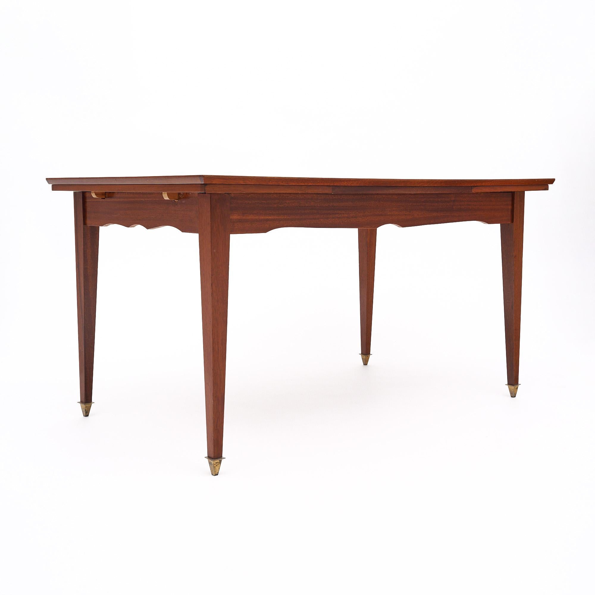 Mid-century dining table from France made of rosewood. This piece features a beautiful rosewood veneer with a stripe of parquetry down the middle of the top. There is a lemon wood inlay detail as well. The legs are all tapered and capped with brass