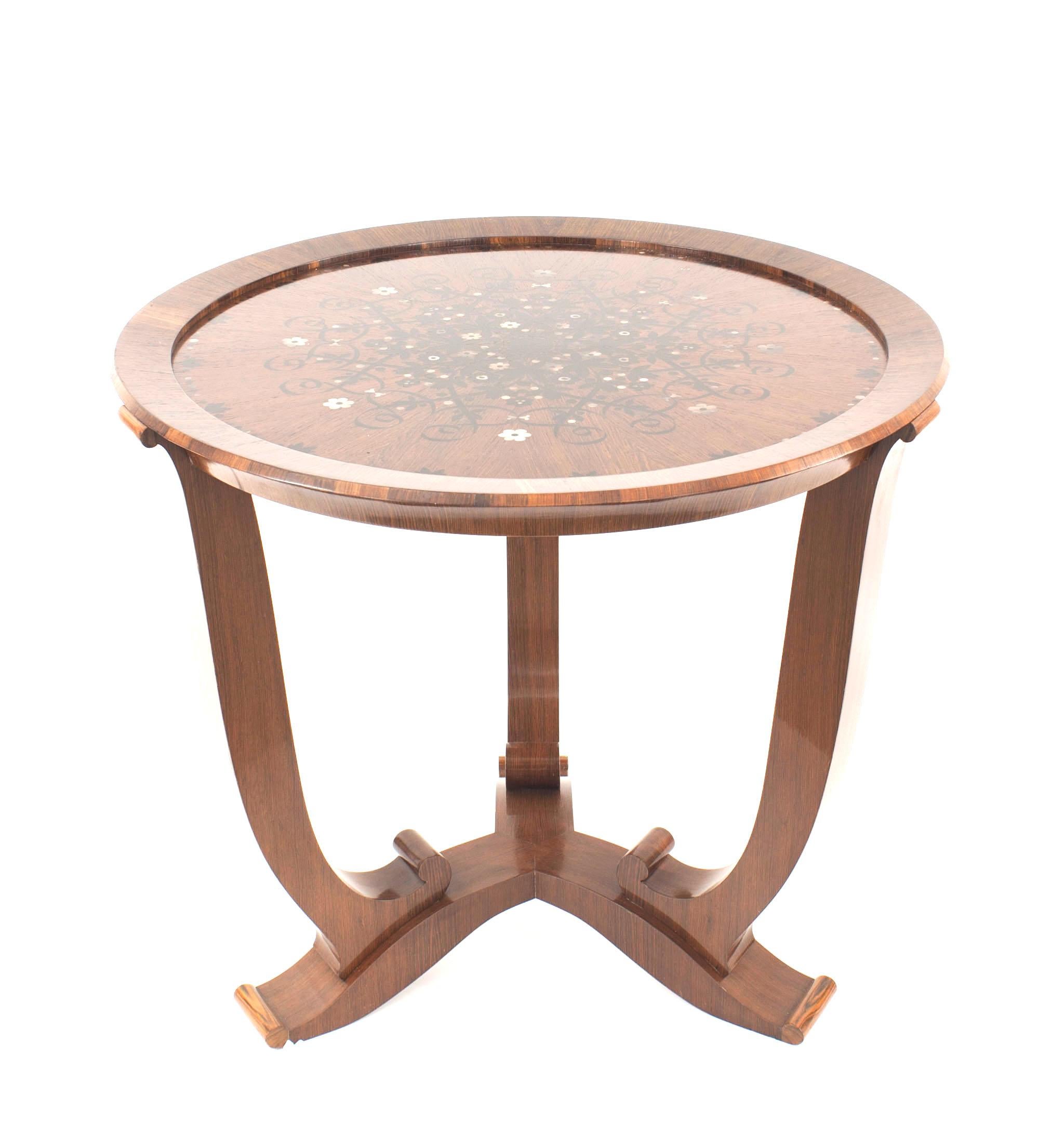 French midcentury rosewood round end table with a floral inlaid top of mother of pearl and ebony supported on three scroll legs connected with a stretcher base (JULES LELEU).


Jules Leleu was a French furniture designer famous for tempering