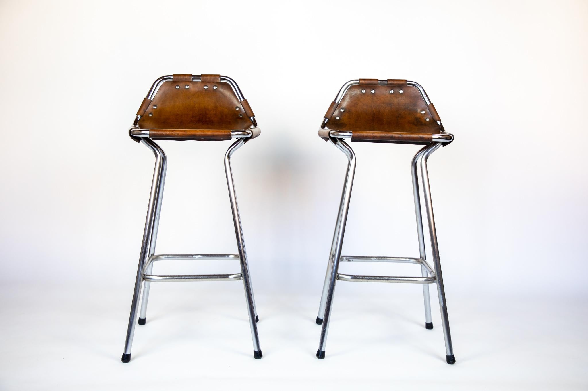 French mid-century saddle leather, brown, chrome bar stools, Perriand, 1960s.

Stunning set of 2 French Mid-Century Modern bar stools designed by the famous Designer Charlotte Perriand for the ski resort „Les Arcs“ in France 1960. The stools have