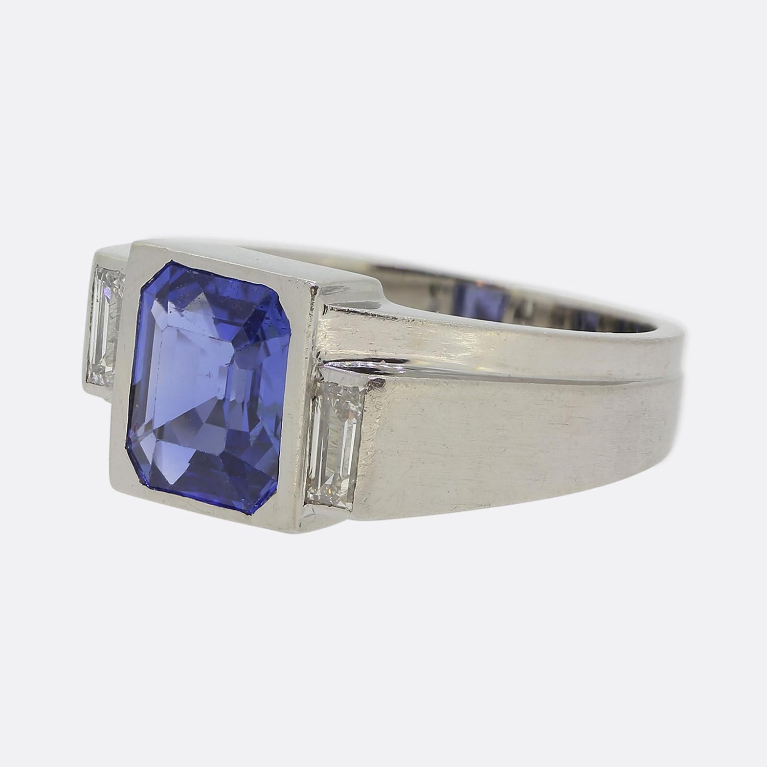 Ecco un elegante e raffinato anello a tre pietre realizzato a metà del XX secolo. Questo gioiello francese in platino mette in evidenza uno zaffiro taglio smeraldo al centro del quadrante, con una tonalità di colore blu naturale. Questa pietra