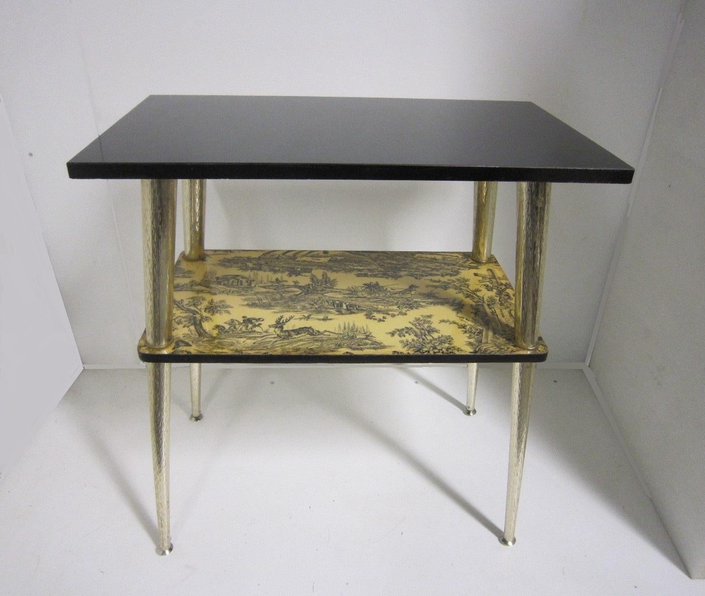A French midcentury console table featuring a black top with toile patterns of a hunting scene on second tier;
the whole raised on slender tapering satin nickel metal legs.
The stretcher shelf is inspired by Toile, a French word meaning 