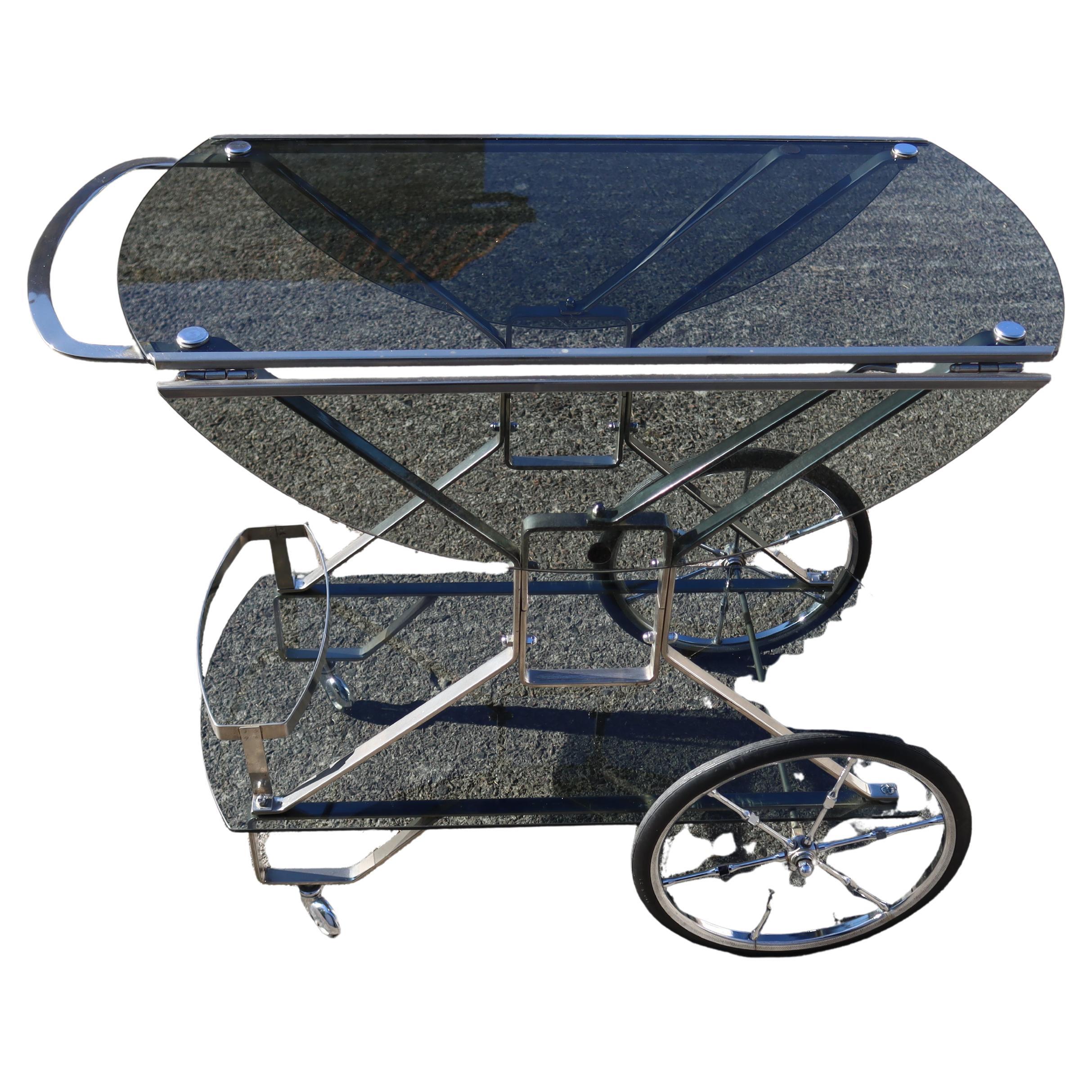 Elegant Vintage Two Tier- Drop Leaf smoked Glass neoclassic Bar Cart from the 60s.
This Drop Leaf Bar Trolley is very rare - it was a wedding present in 1965.
The upper Serving Surface can be easily enlarged to a maximum of twice its width by