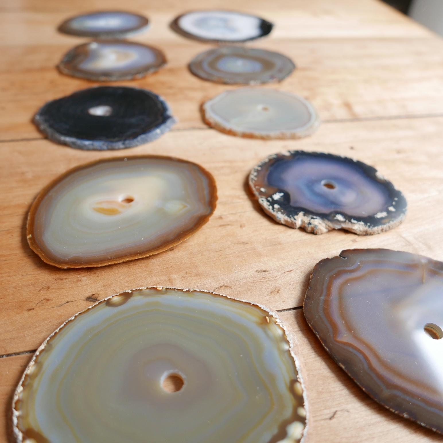 A set of natural stone circular drink place mats or coasters. Likely Agates.

France, c1970s.

A variety of colours and stone specimens.

All have a circular hole in the centre presumably to mount on a rod for storage. But said rod is