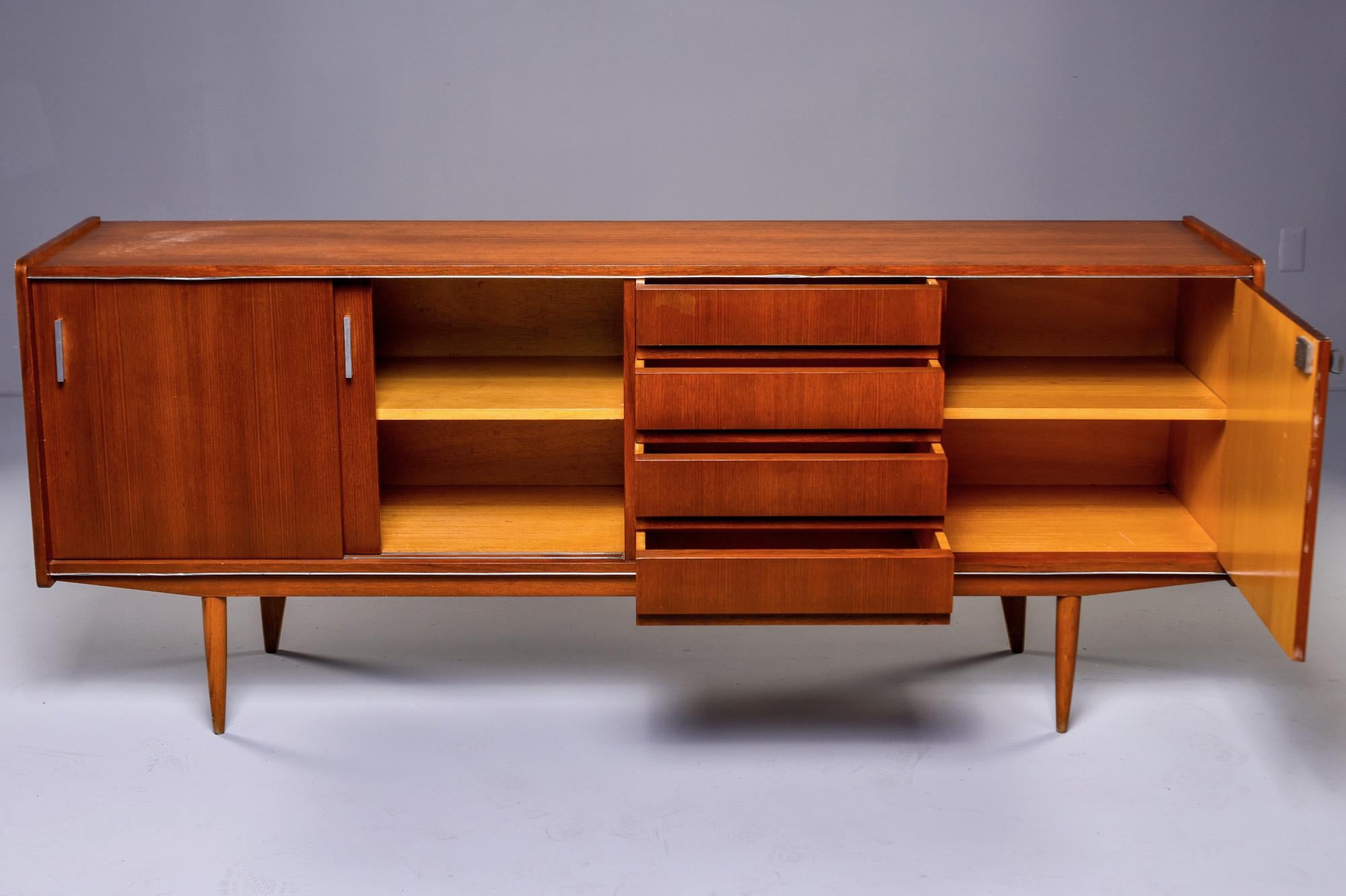 Circa 1960s French teak wood buffet or credenza with section of four drawers with dovetail construction flanked by storage compartment with hinged door and a larger compartment with sliding doors and single internal shelf. Tapered legs. Unknown