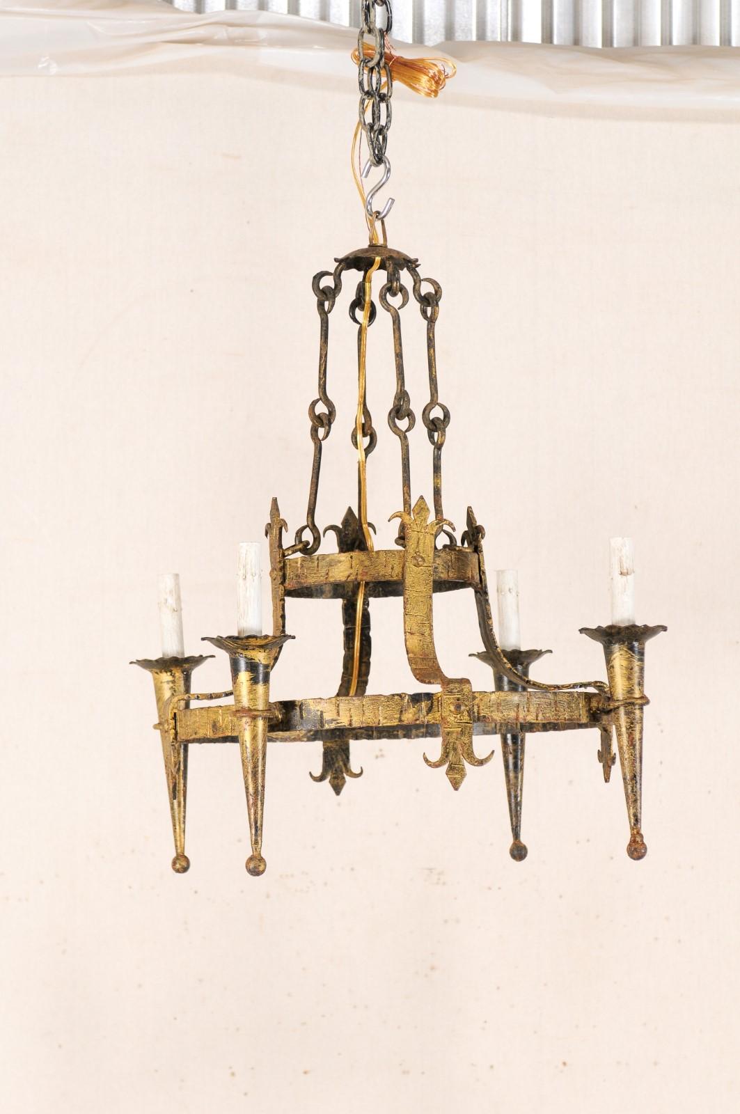A French double-ringed gold-tone iron chandelier with four lights and Fleur di Lis motif from the mid-20th century. This mid-20th century chandelier from France features a double ringed central gallery, with the larger lower ring supporting four