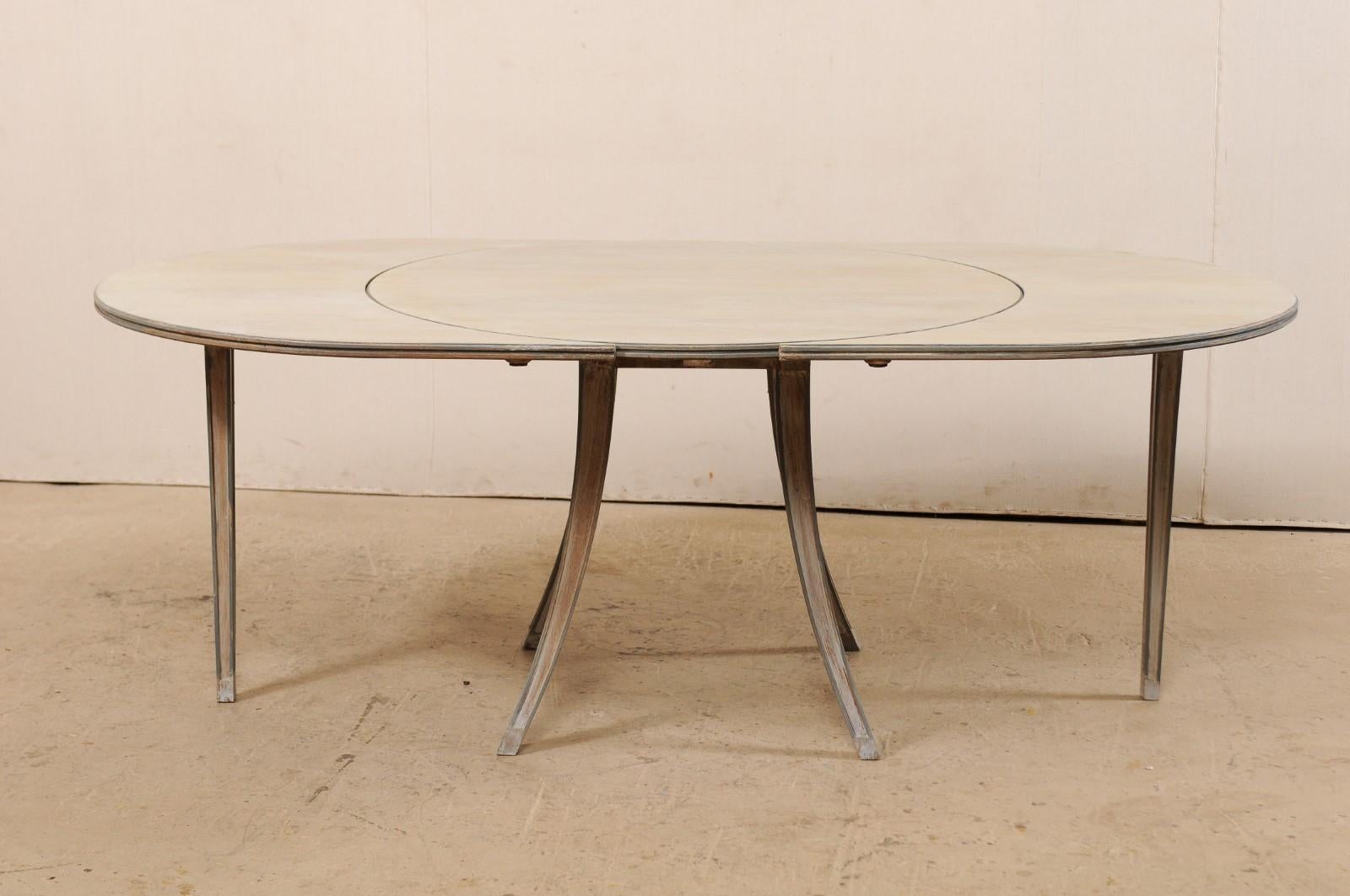 A French Mid-Century Modern oval-shaped painted-wood table with side leaves. This unique table from France features an overall oval-shape with side leaves attached, which when removed, transitions this piece into a circular center table. The design
