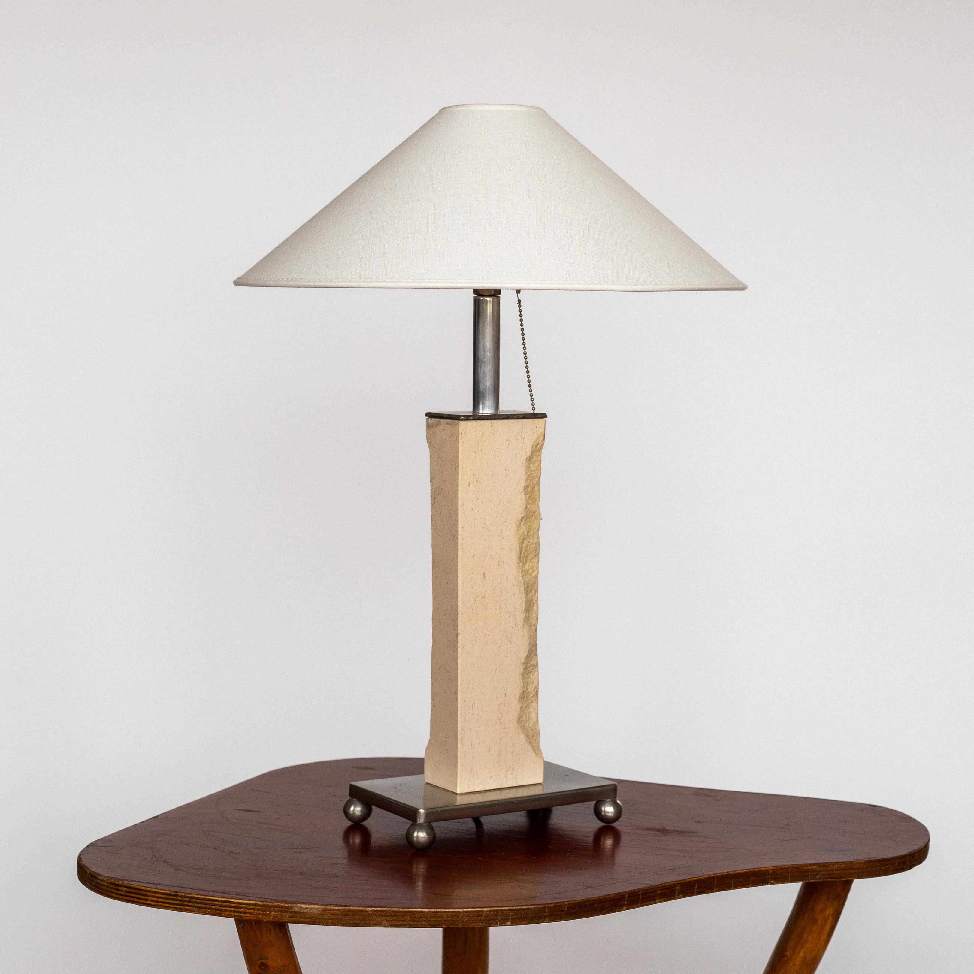 Esta notable lámpara de sobremesa francesa de mediados del siglo XX presenta un gran e impresionante cuerpo rectangular de travertino que descansa sobre una base rectangular de metal con pies de bola. 

Un diseño escultórico inusual en el que dos