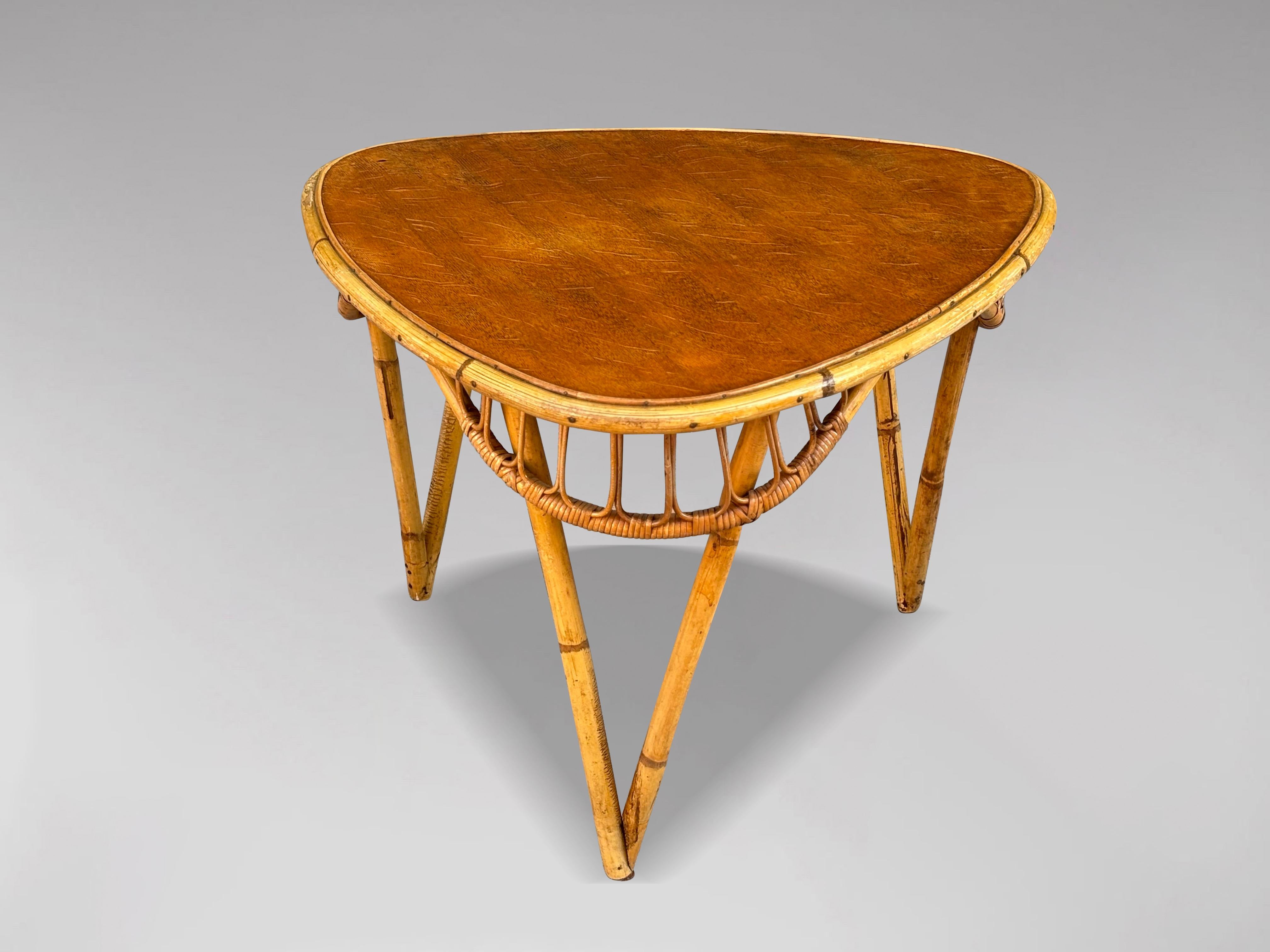 Cette table d'appoint ou table basse en bambou et rotin de la Côte d'Azur du milieu du XXe siècle présente un cadre triangulaire en bambou avec du rotin tressé à la main. La table présente une belle couleur et une patine sur le plateau triangulaire,