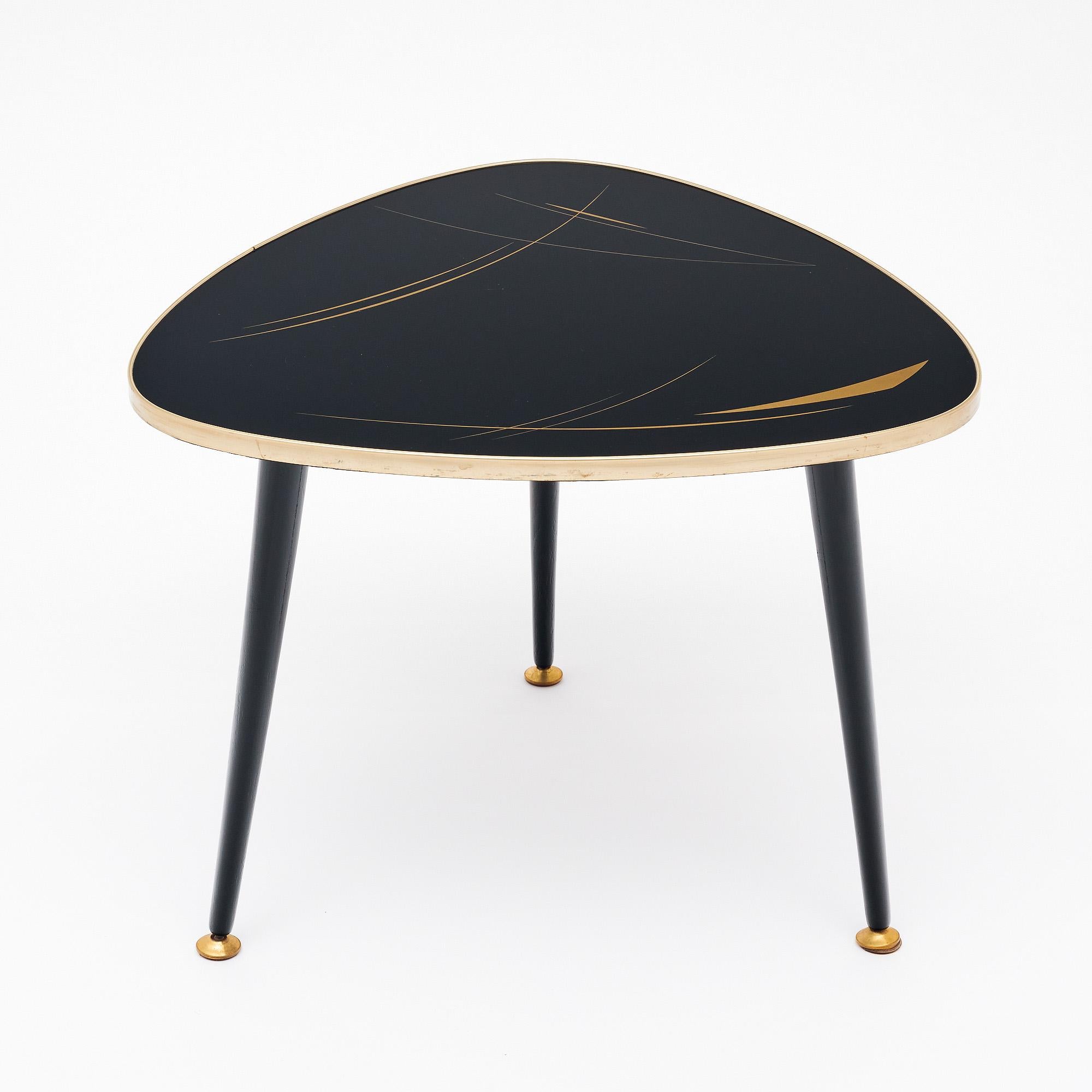 Table d'appoint du milieu du siècle en France, avec un design tripode. Le plateau est triangulaire avec des bords incurvés et est garni de laiton. La partie supérieure triangulaire est noire avec des détails dorés. Les pieds coniques noirs sont