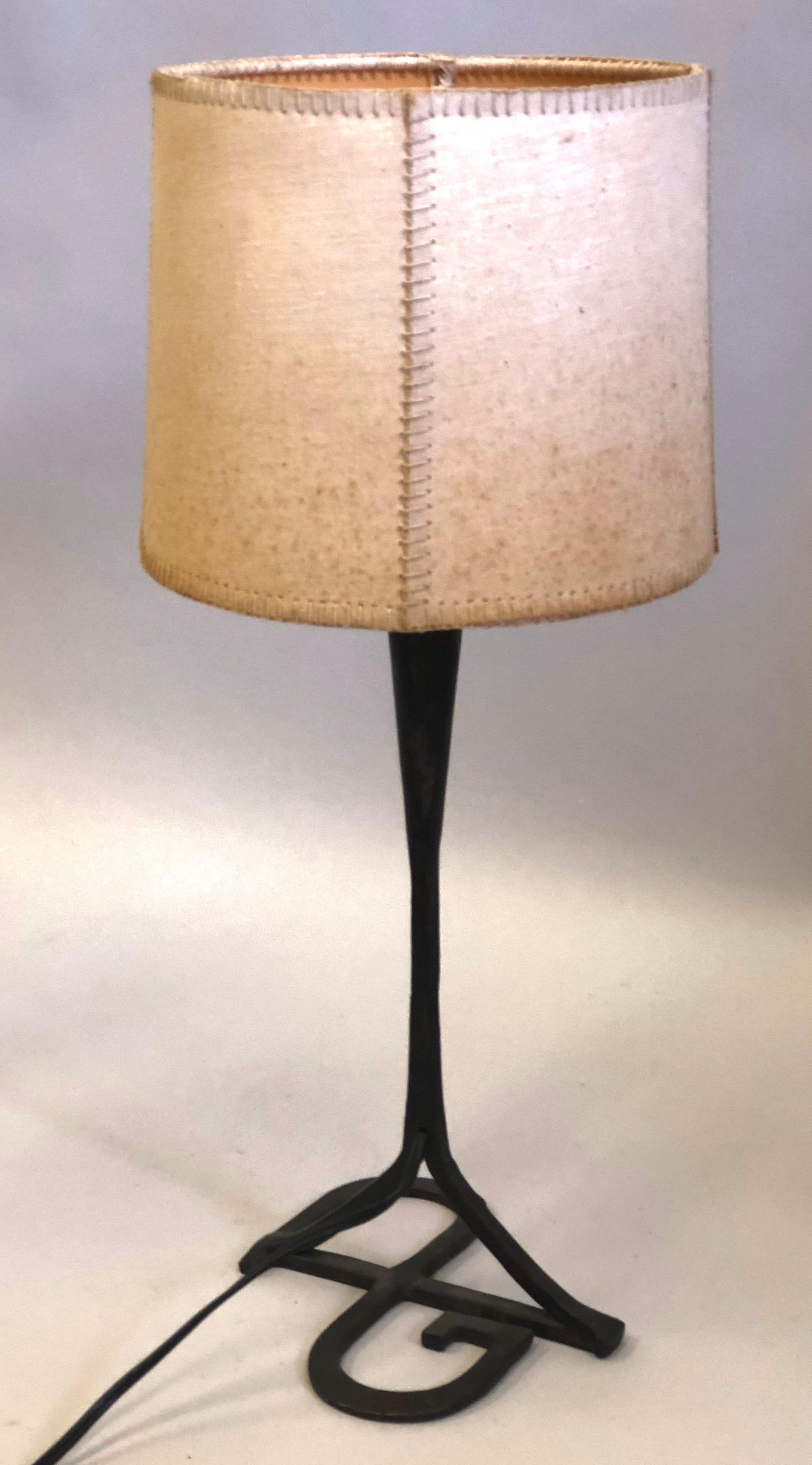 An Elegant, hand made, Unique French Mid-Century Modern table lamp or desk lamp in hand forged and hand-hammered iron with a parchment shade attributed to Gilbert Poillerat. The base is formed with the unity of the initials GP which stands for the