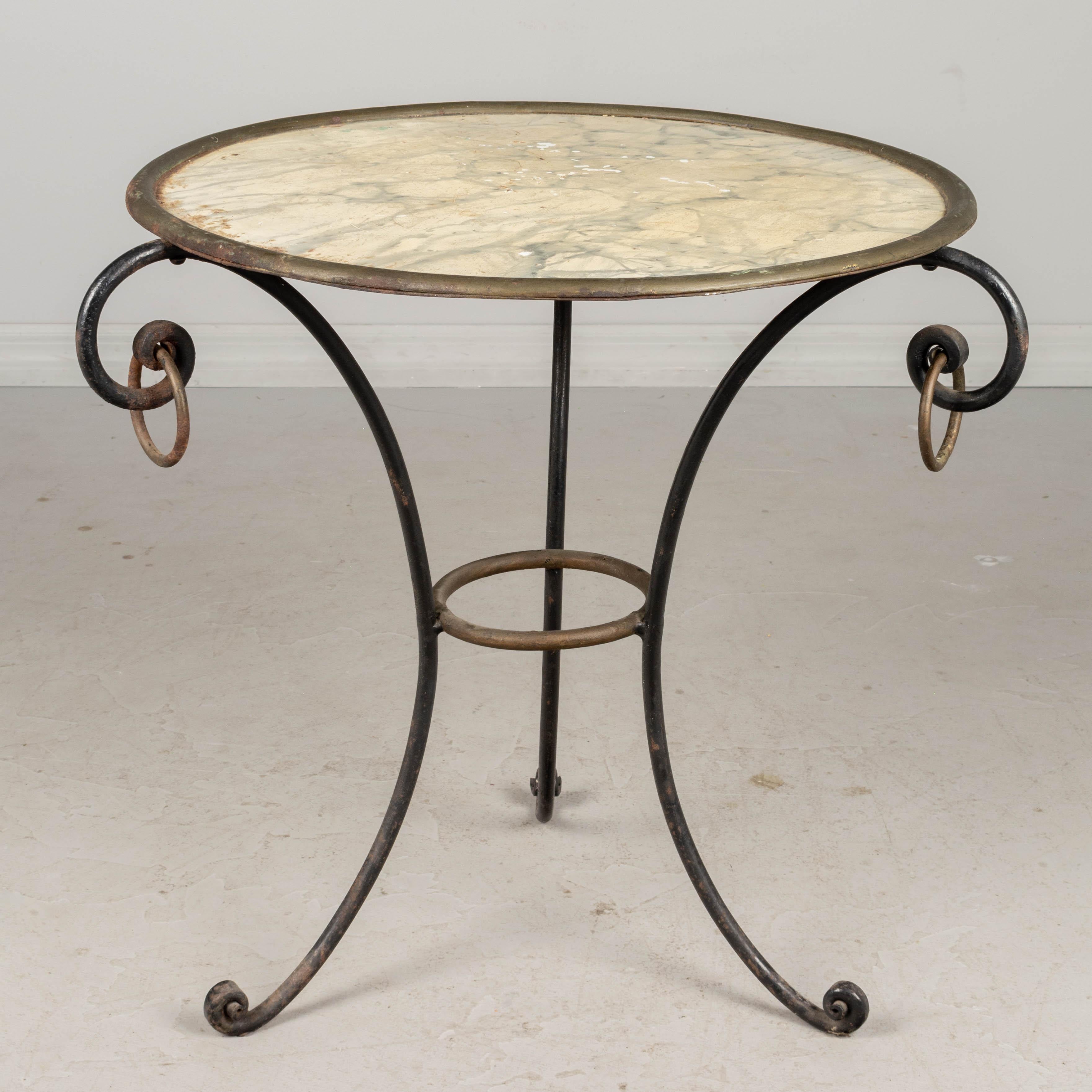 A French mid century wrought iron side table with faux marble painted tole top. Black tripod base with large decorative rings. Painted surface is slightly worn with some paint loss and rust spots. Please refer to photos for more details. Pictures