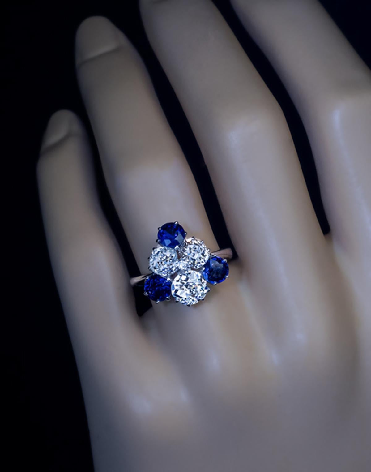 A mid century (circa 1950) 18K white gold cluster ring is designed as a stylized flower set with three chunky old brilliant cut diamonds accented by three deep blue natural sapphires. A small single cut diamond is set between the three bigger
