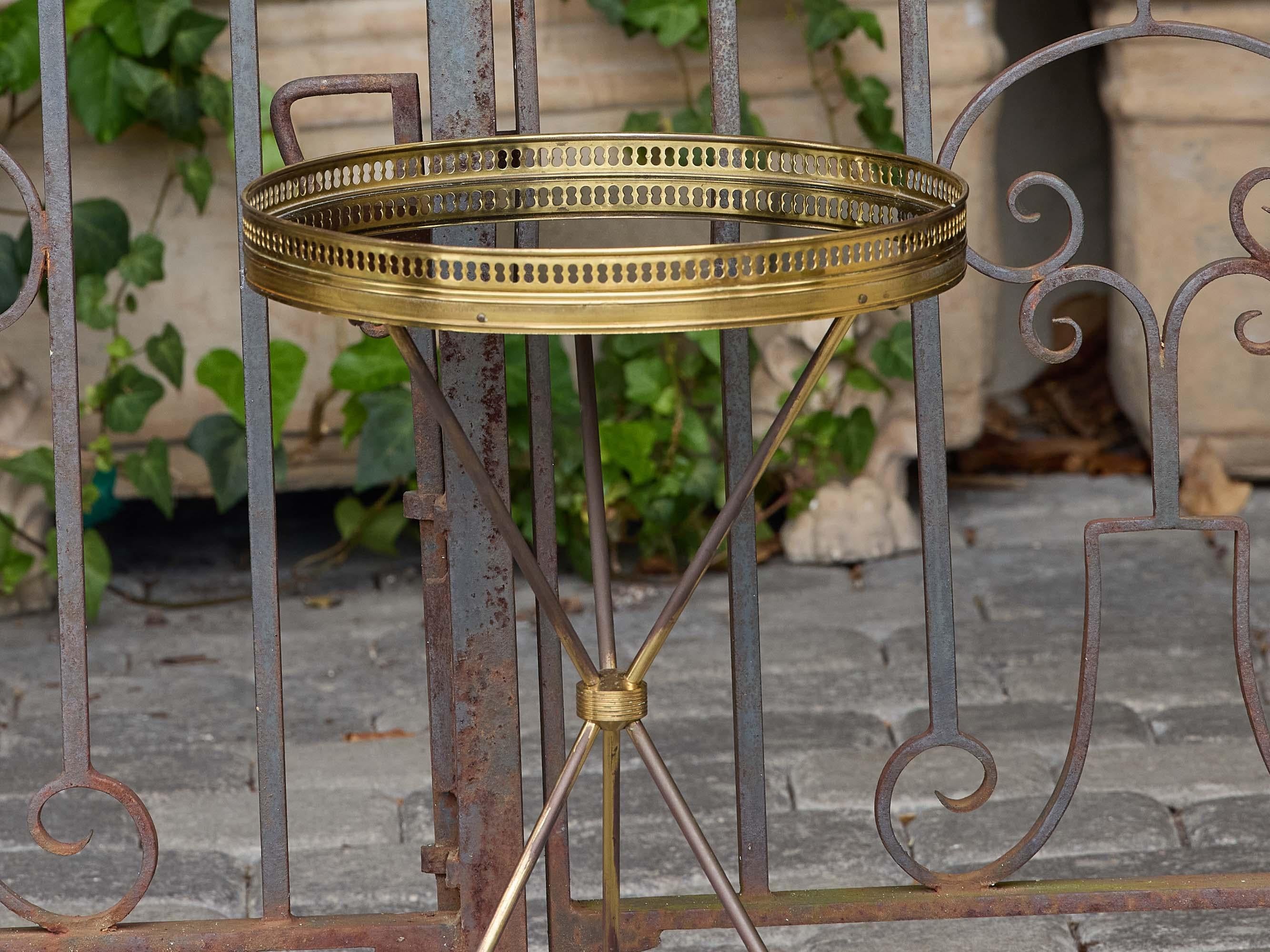 A refined French midcentury gueridon table crafted entirely in brass. The circular top is inset with mirror, framed by a pierced brass gallery that adds both elegance and function. The slender tripod base is joined at center with a brass collar and