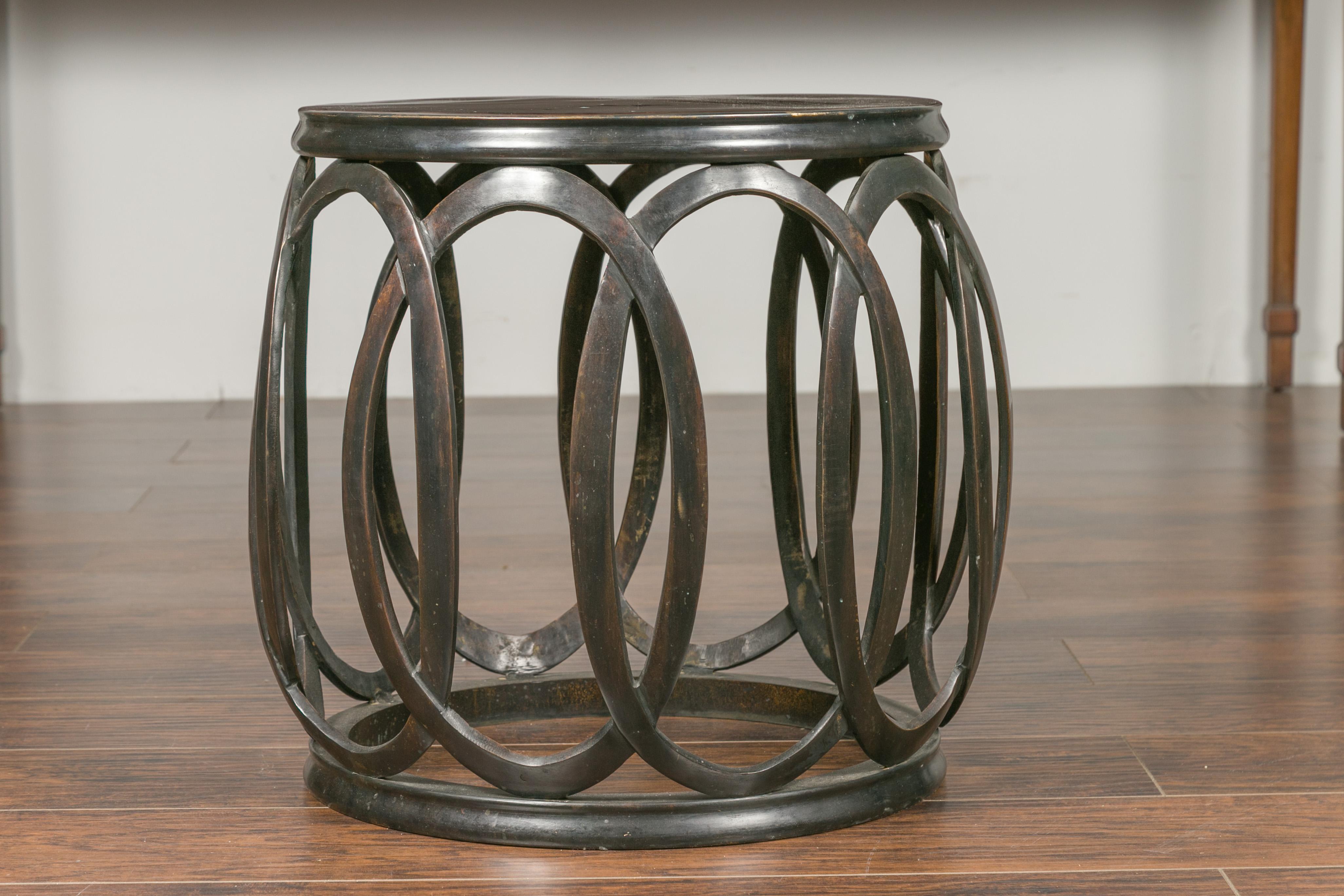 A French vintage bronze drum drinks table from the mid-20th century with intertwining oval motifs. Born in France during the midcentury period, this bronze drum table features a circular top sitting above an interesting base presenting intertwining