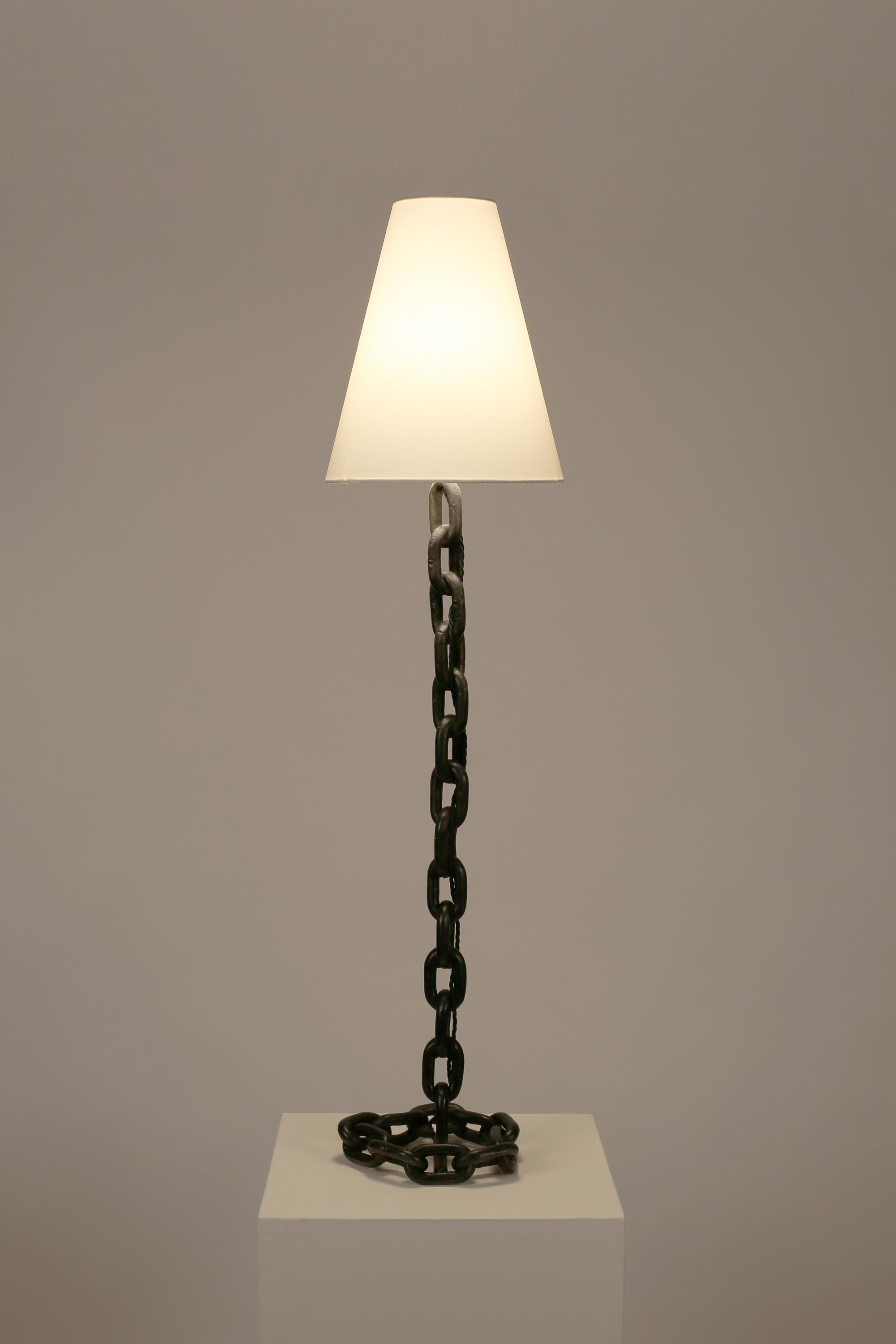 A large welded iron chain link table/half-height floor lamp with black enamel finish and ‘coiled’ base. French, c. 1950s. Supplied with a bespoke white cotton cone shade.

Rewired for the UK and PAT tested.