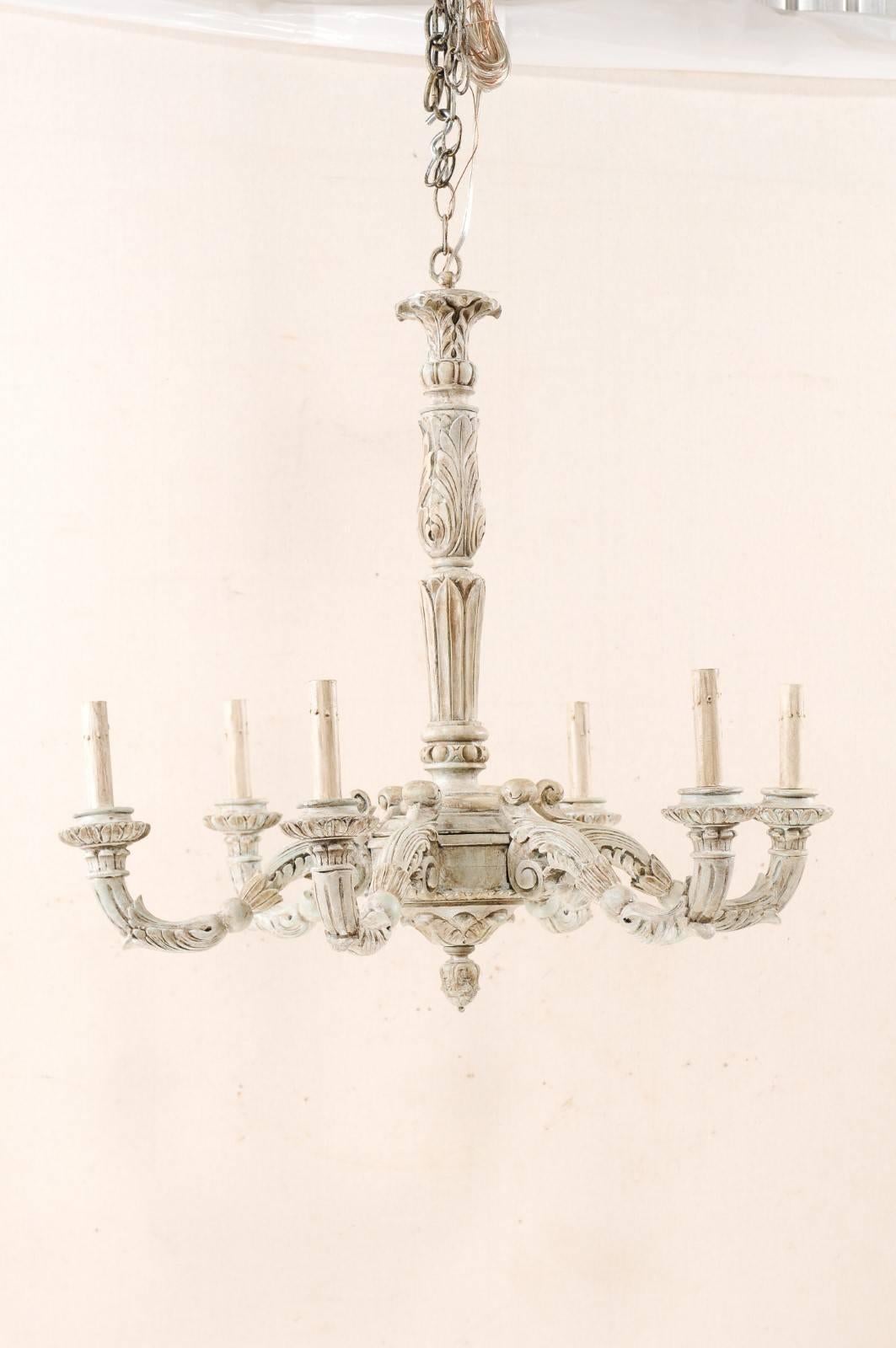 A French six-light painted and carved wood chandelier with scroll arms and wood bobèches. This French mid-20th century chandelier features a central wood column, with carved foliage motif, terminating into a carved bottom final. The S-scroll arms,