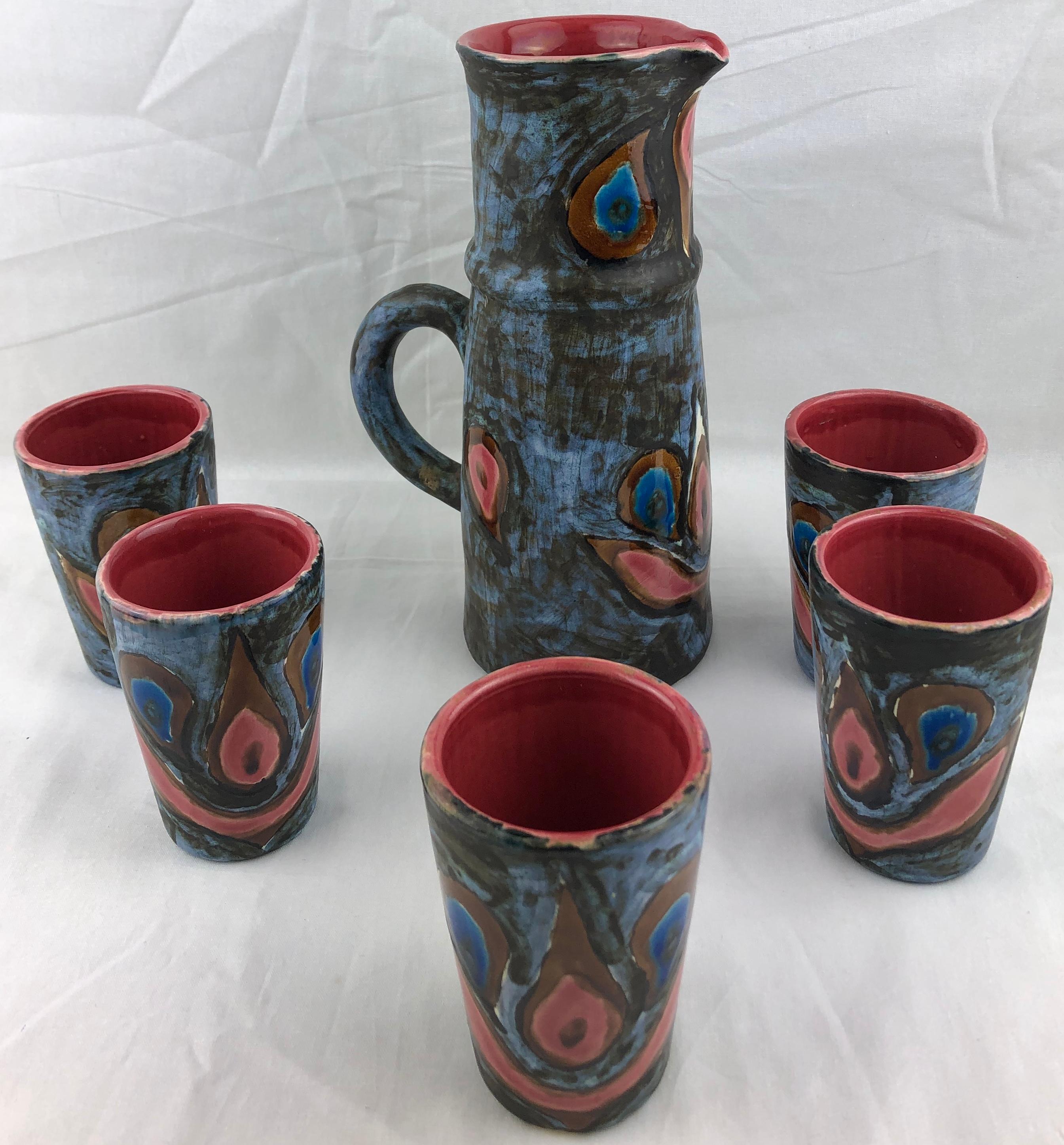Pichet et cinq tasses en céramique magnifiquement travaillés et aux couleurs étonnantes.
Fabriqué à la main à Vallauris, en France, selon des techniques de poterie traditionnelles, vers le milieu des années 1950. 
Le plus souvent utilisé comme