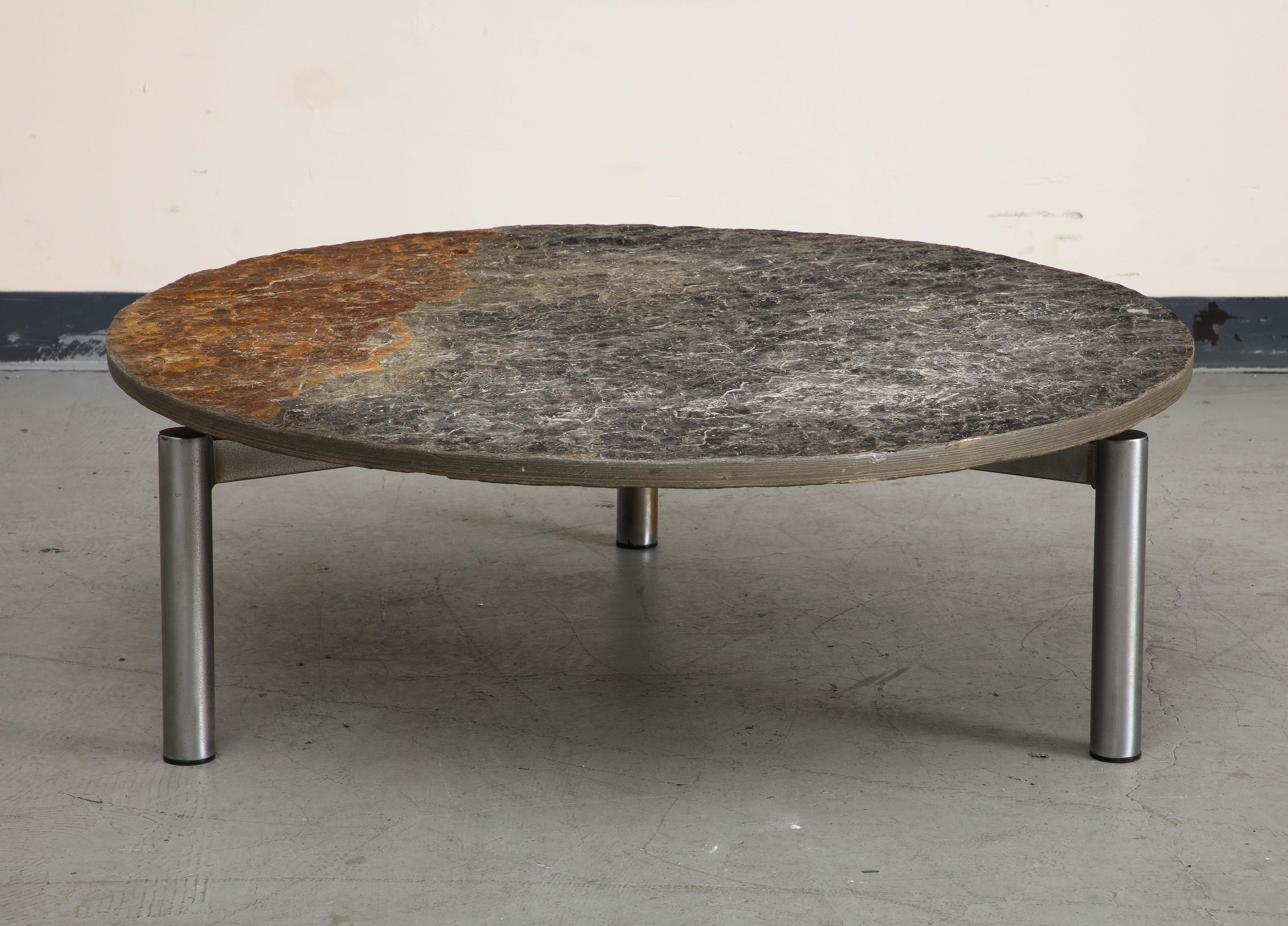 Table basse française du milieu du siècle avec base en acier chromé. Trois pieds cylindriques en acier soutiennent le plateau rond en ardoise naturelle, qui présente une certaine oxydation. 

