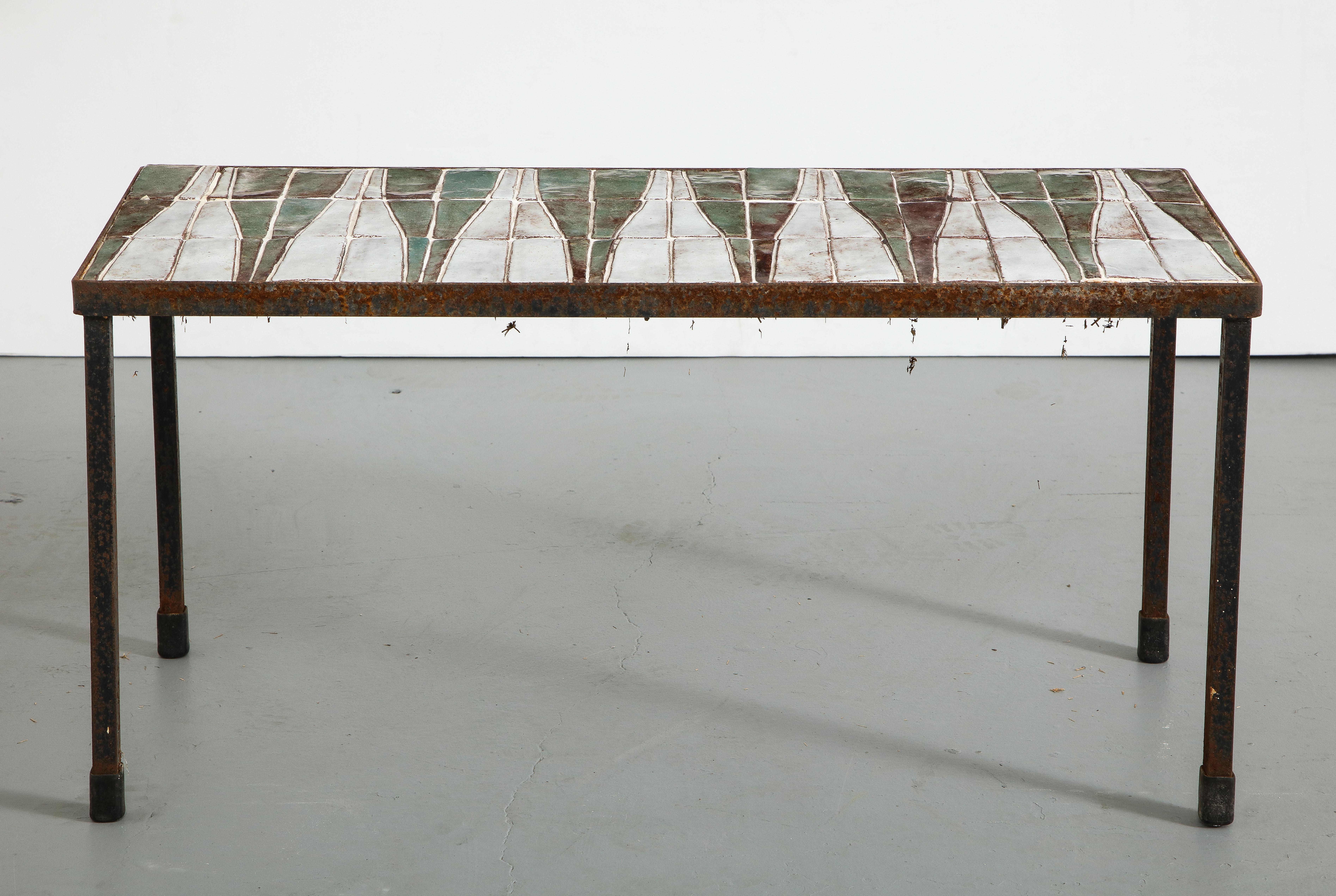 French midcentury coffee table with ceramic tile top. Green and white ceramic tiles form a large triangle pattern across the surface with variations on the individual tiles. Metal frame/legs show oxidation/rust from outdoor use.