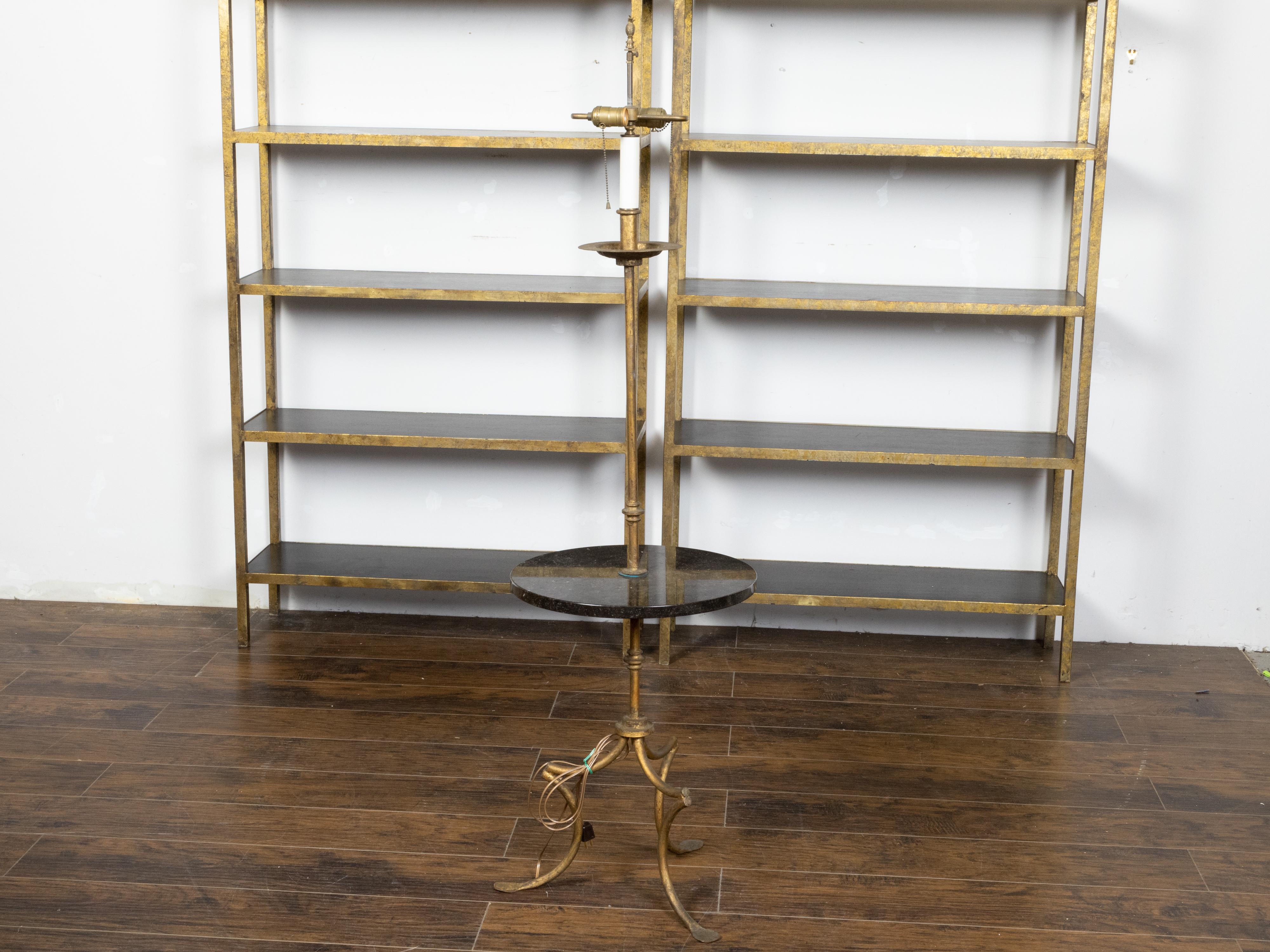 A vintage French gilt iron floor lamp guéridon table from the mid 20th century, with black granite top, two lights and curving tripod base. Created in France during the Midcentury period, this unusual item charms us with its great versatility. A