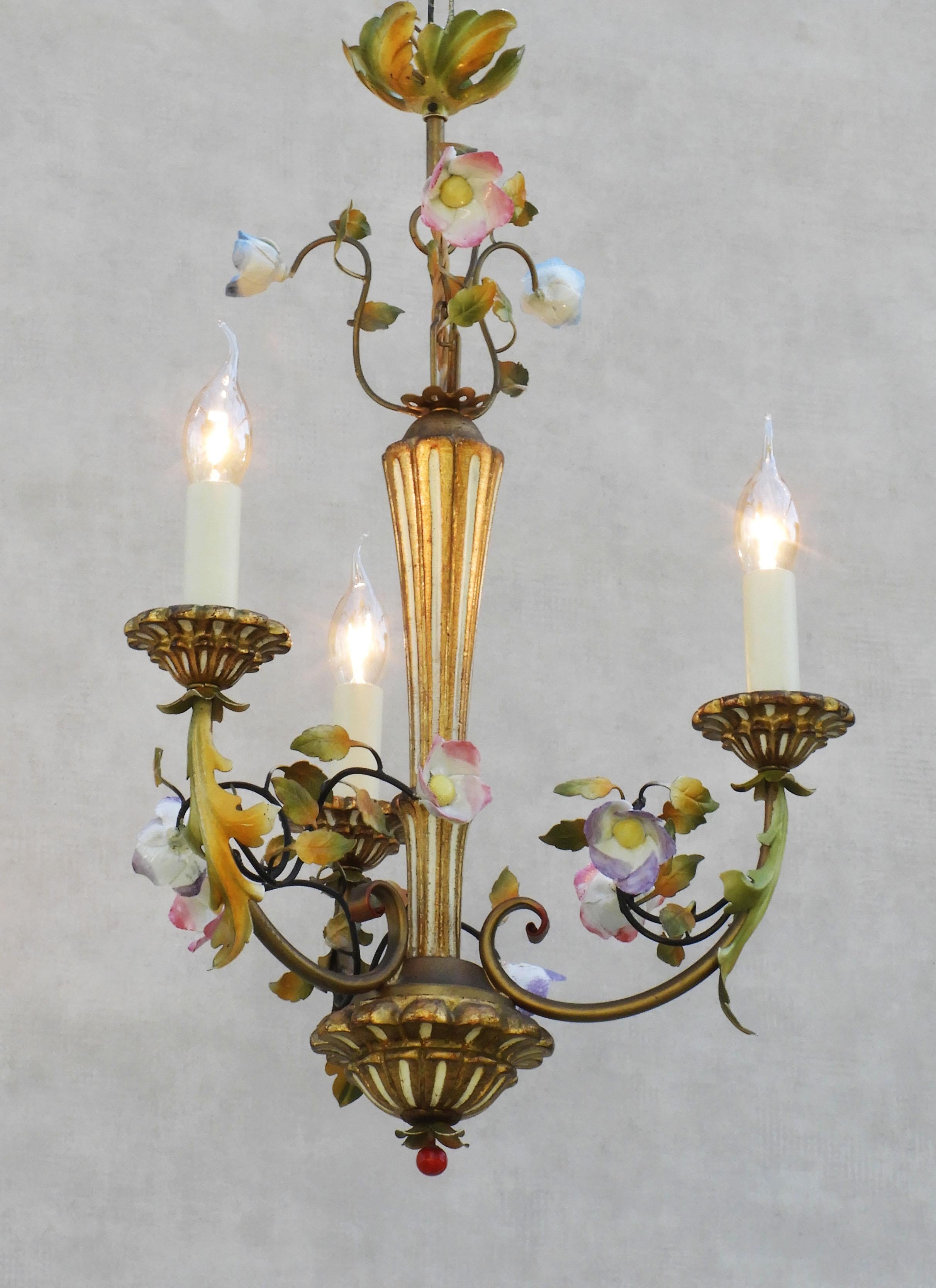 A charming French midcentury giltwood and painted tole pendant light chandelier with hand-crafted porcelain flowers. Three 'faux' candle lights on carved and gilded 'bobeches', nestling amongst green and gold foliage, surrounding a central carved