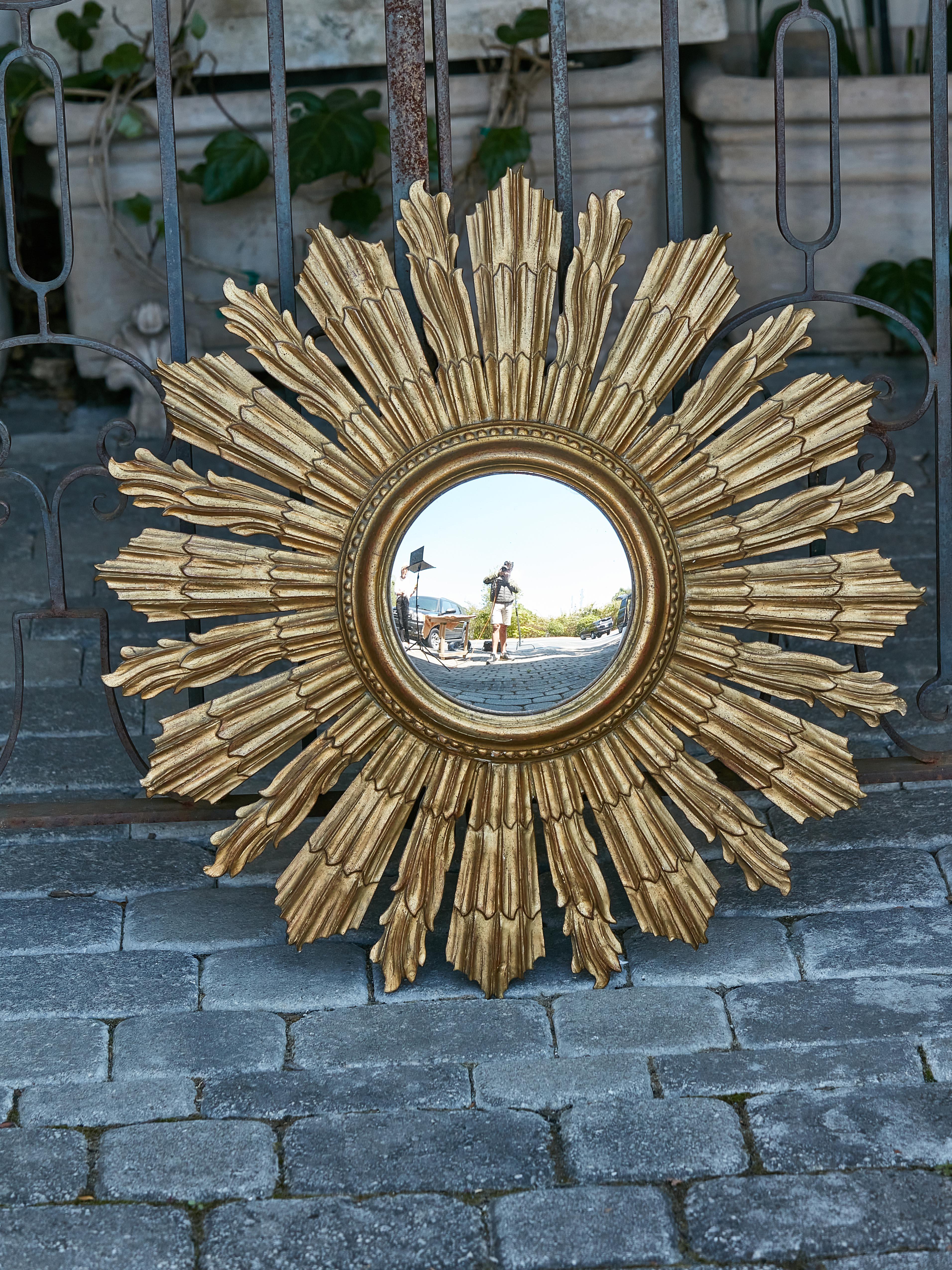 A French giltwood sunburst mirror from the Midcentury period with convex mirror plate surrounded by petite carved beads and sun rays lon two levels alternating straight and wavy lines. Bathing your space in a golden aura, this French giltwood