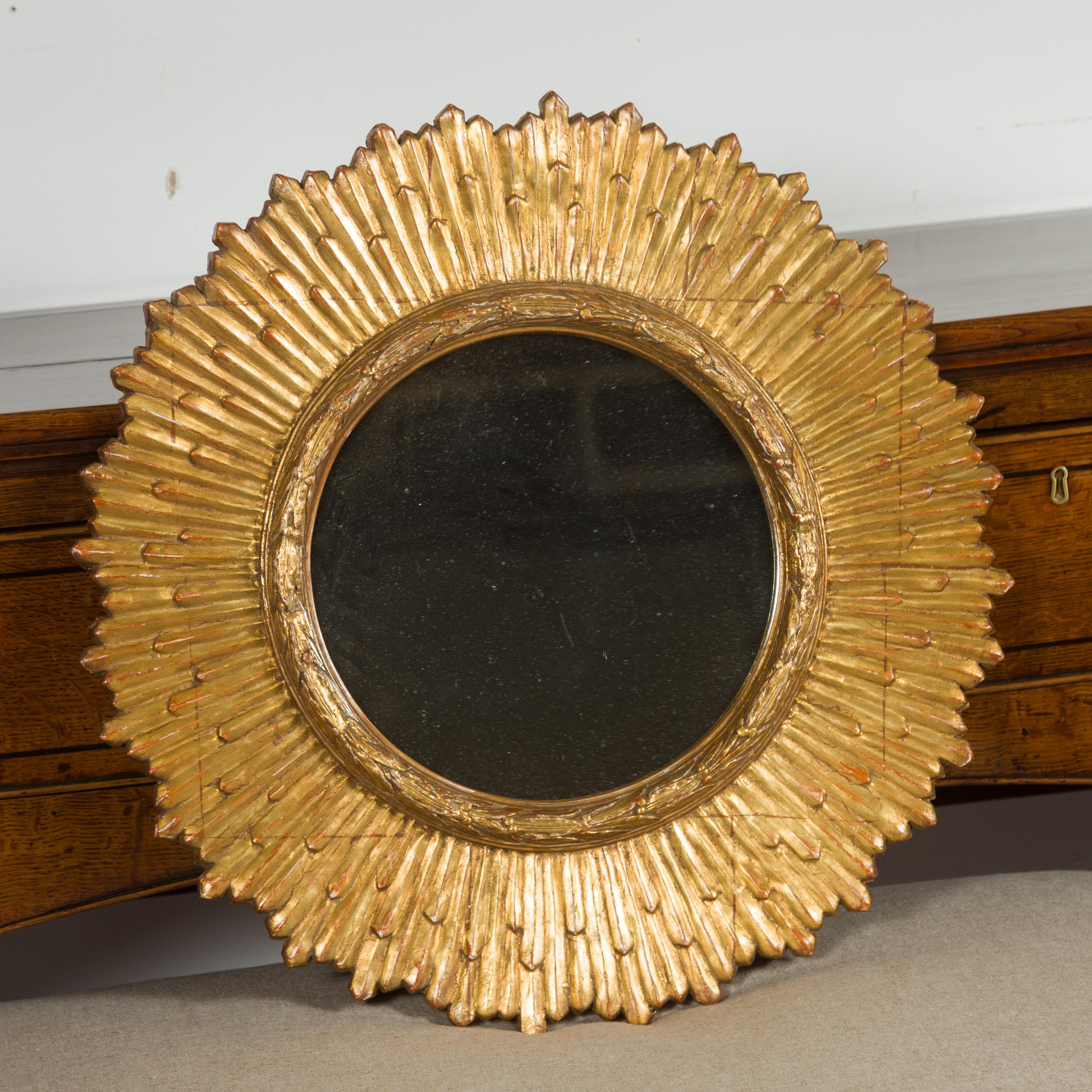 A French vintage giltwood sunburst mirror from the mid-20th century, with rays of slightly varying sizes, carved frame and red undertone. Born in France during the mid-century period, this sunburst mirror features a clear mirror plate surrounded by