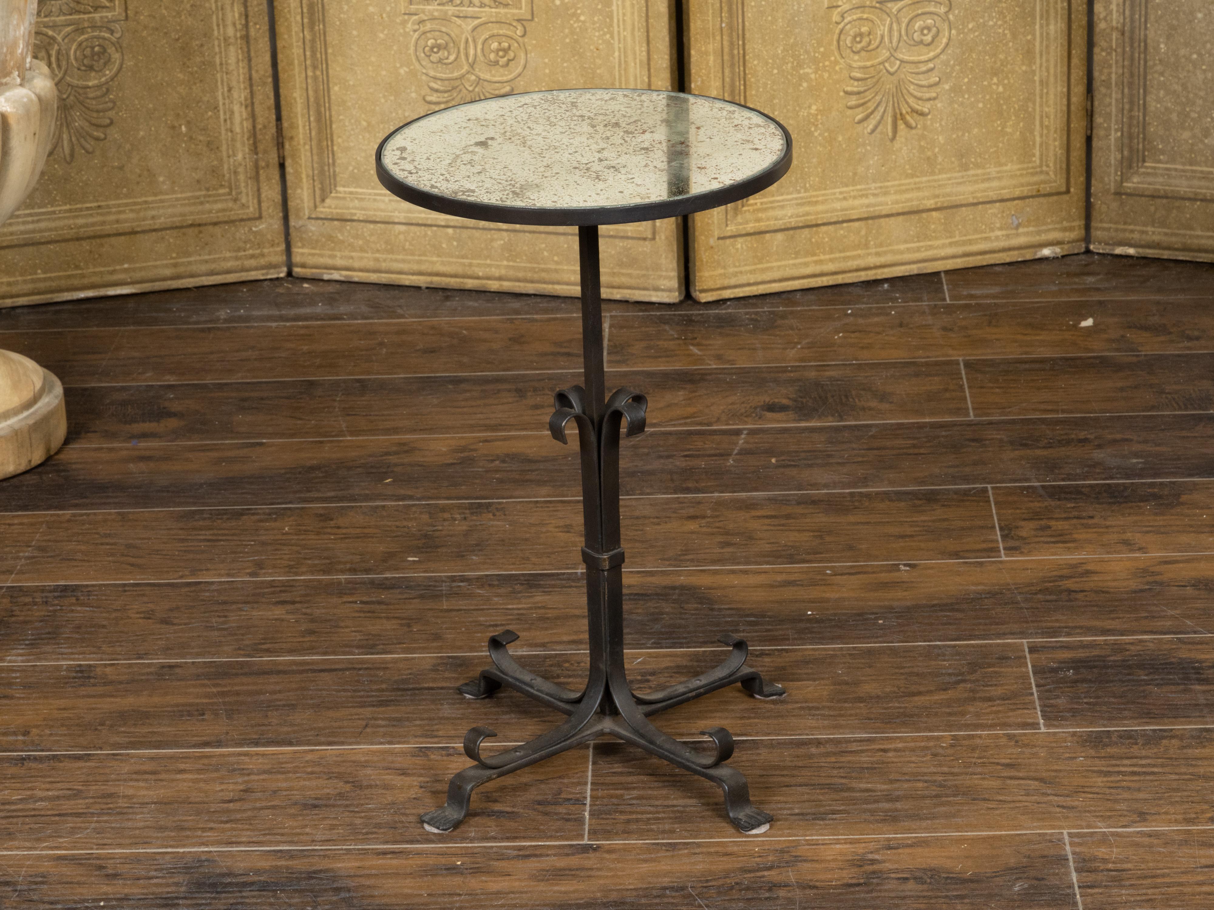 A vintage French iron side table from the mid 20th century, with antiqued circular mirrored top and quadripod base. Created in France during the Midcentury period, this iron side table features a circular mirrored top with heavily antiqued finish,