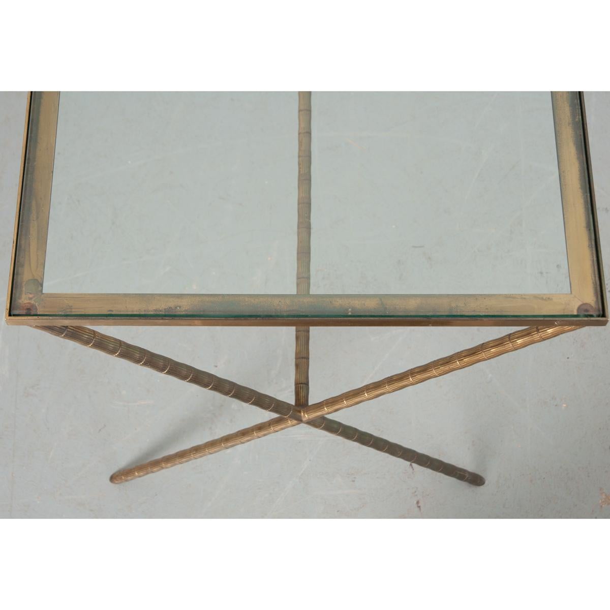 A vintage French (mid-20th century) Maison Jansen style rectangular occasional table with faux-bamboo brass base and clear glass top. The removable glass surface is inset to be flush with the frame, protected by a low trim and rising from X-shaped
